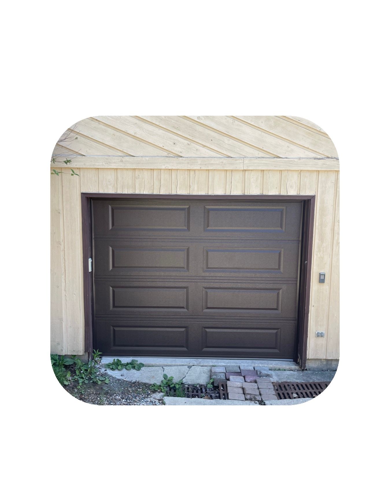 Brown garage door, surrounded by light-colored siding, and a small walkway in front.