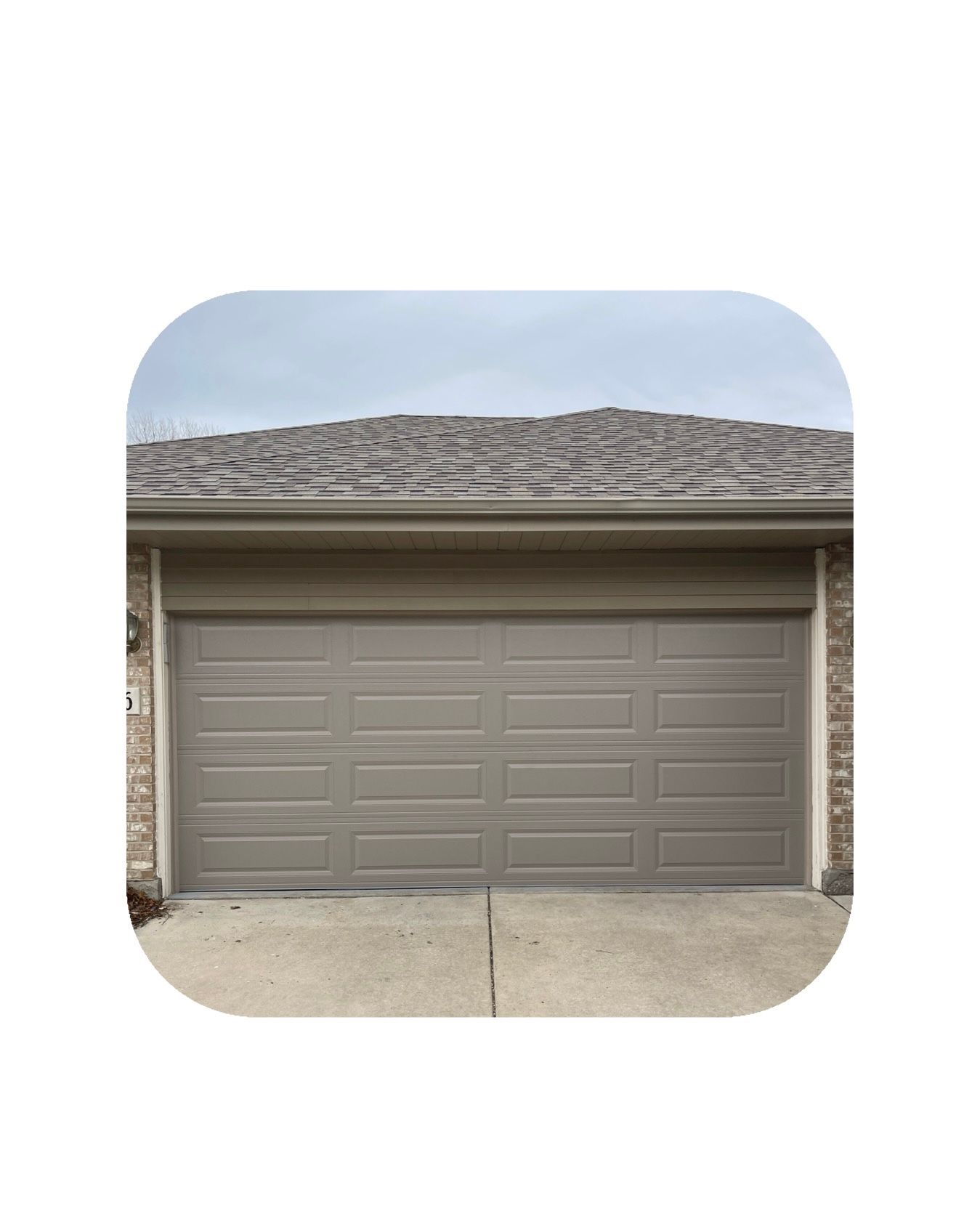 Tan garage door on a house with a gray roof and driveway, under a cloudy sky.