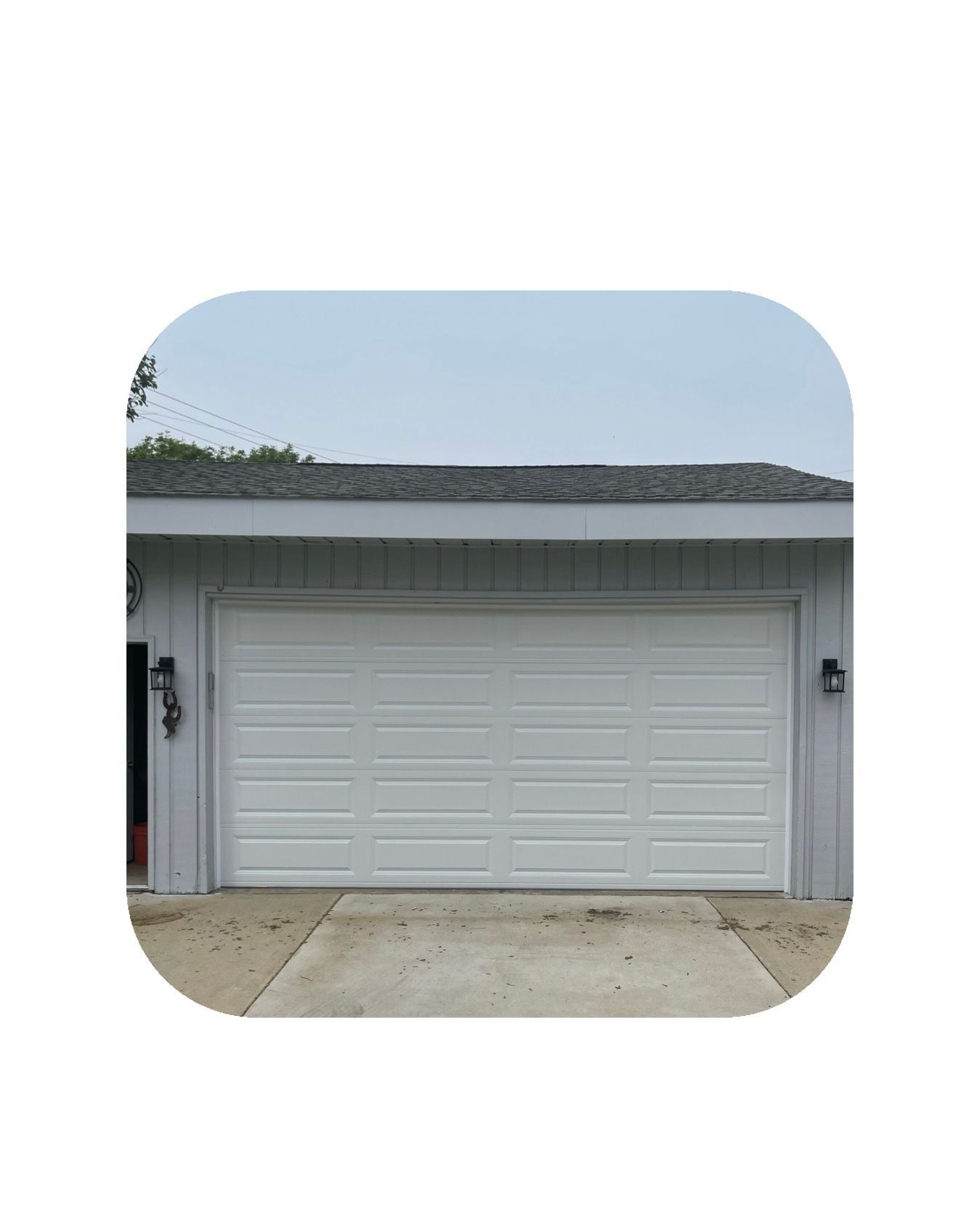 White garage door, light grey building, driveway, and blue sky.