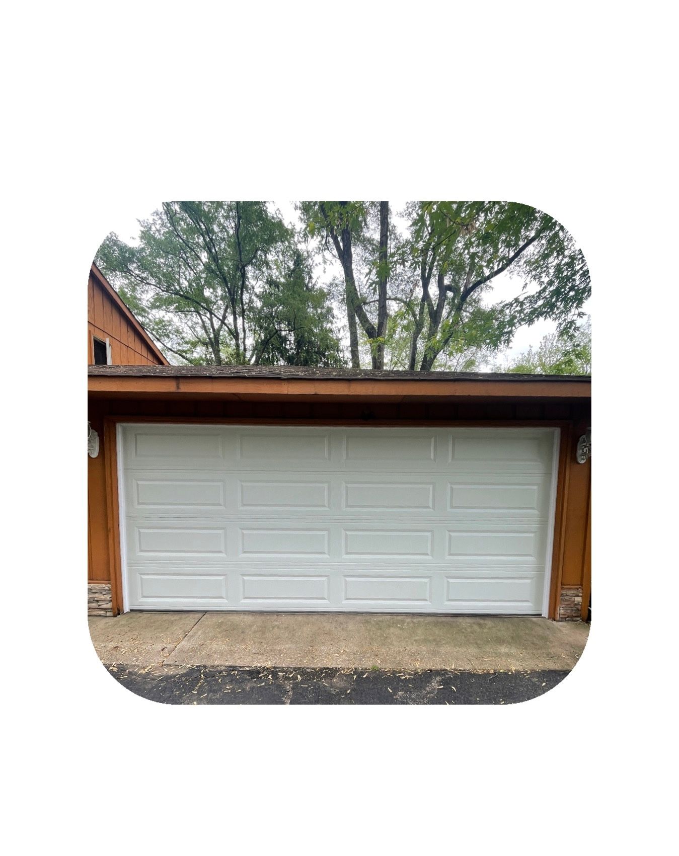 White garage door on a brown building with trees in the background.