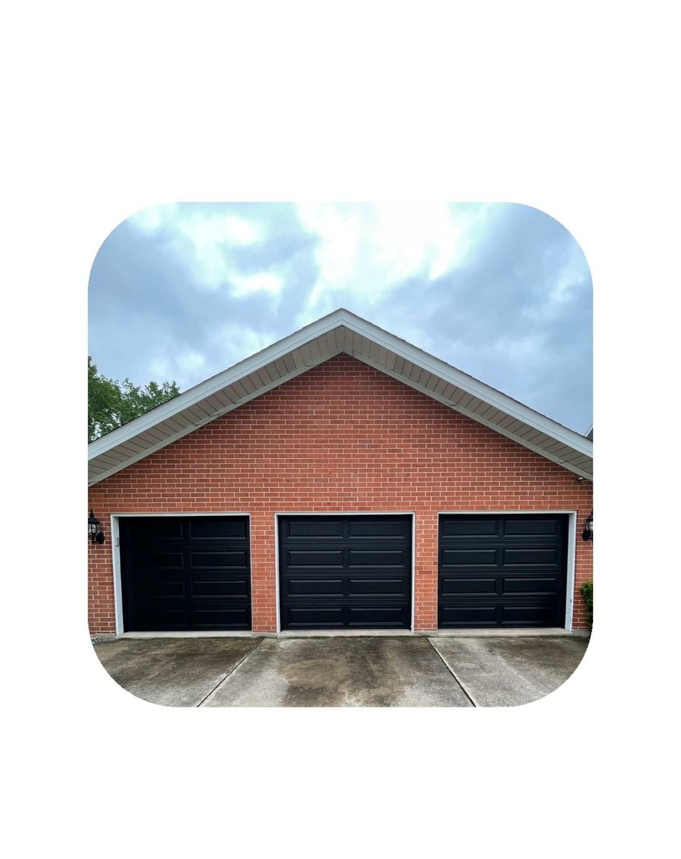 Three-car garage with black doors and red brick facade under a cloudy sky.