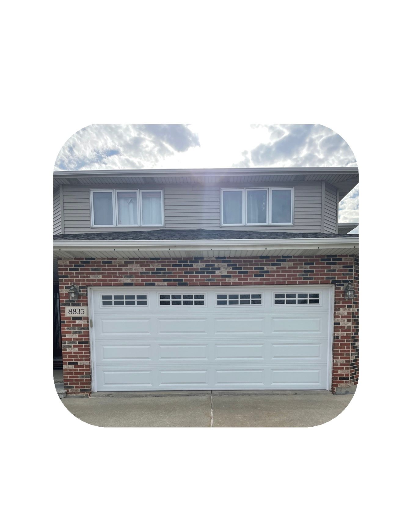 Two-story house with a white garage door, red brick facade, and grey siding; cloudy sky overhead.