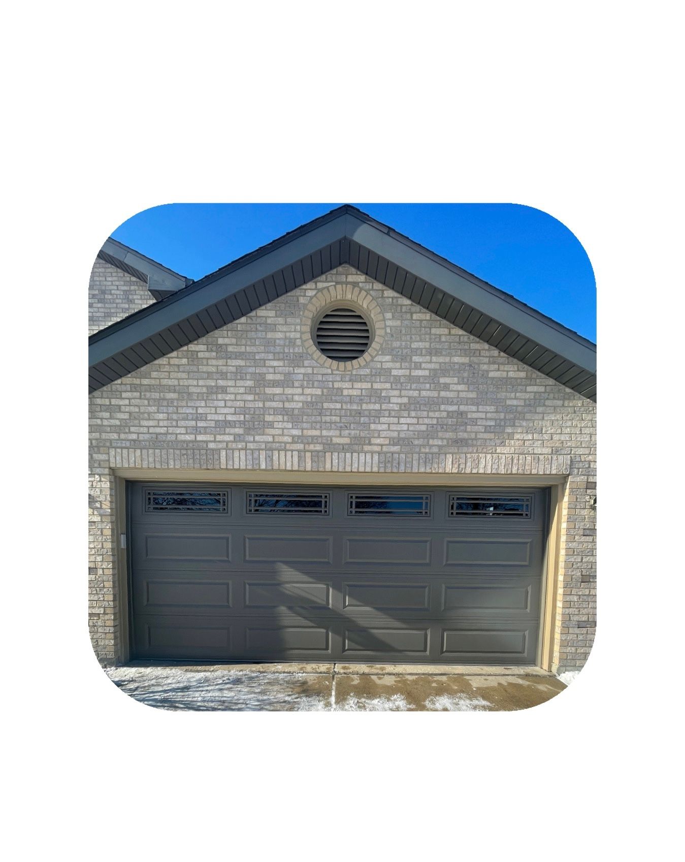 Gray garage door beneath gray brick facade with round vent and blue sky.