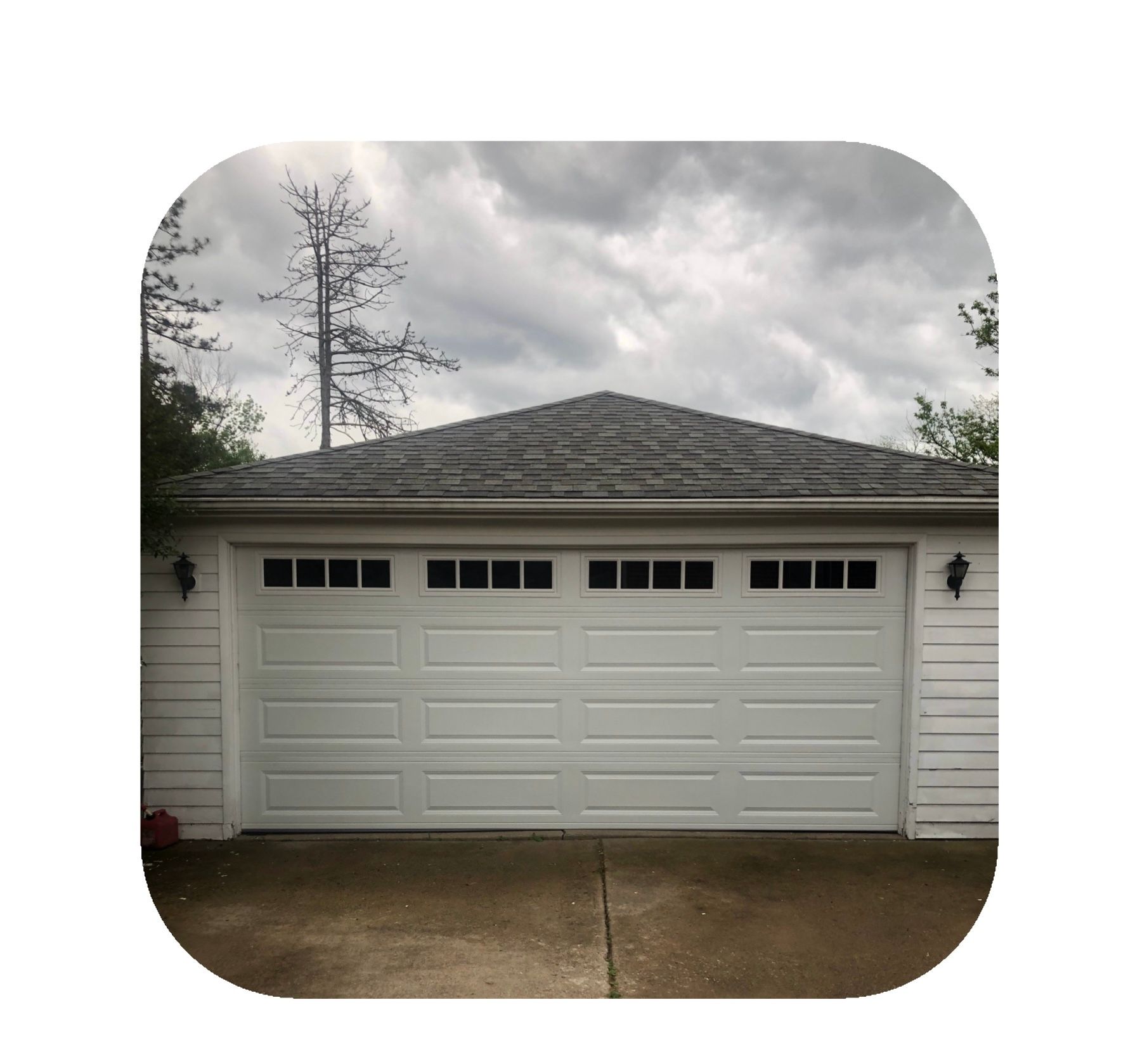 White garage with black-shingled roof under a cloudy sky.