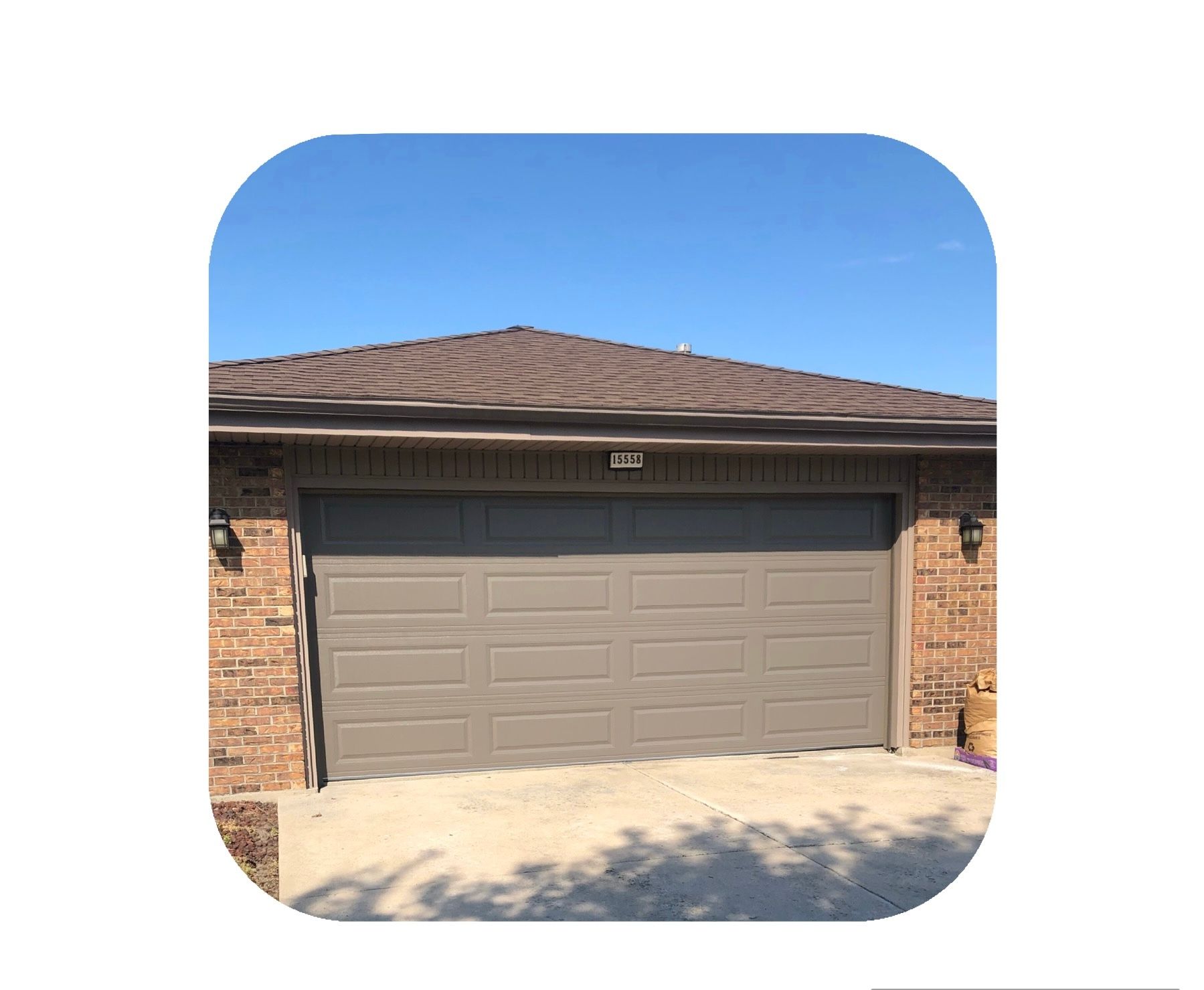 Tan garage door on a brick building with a brown roof under a blue sky.