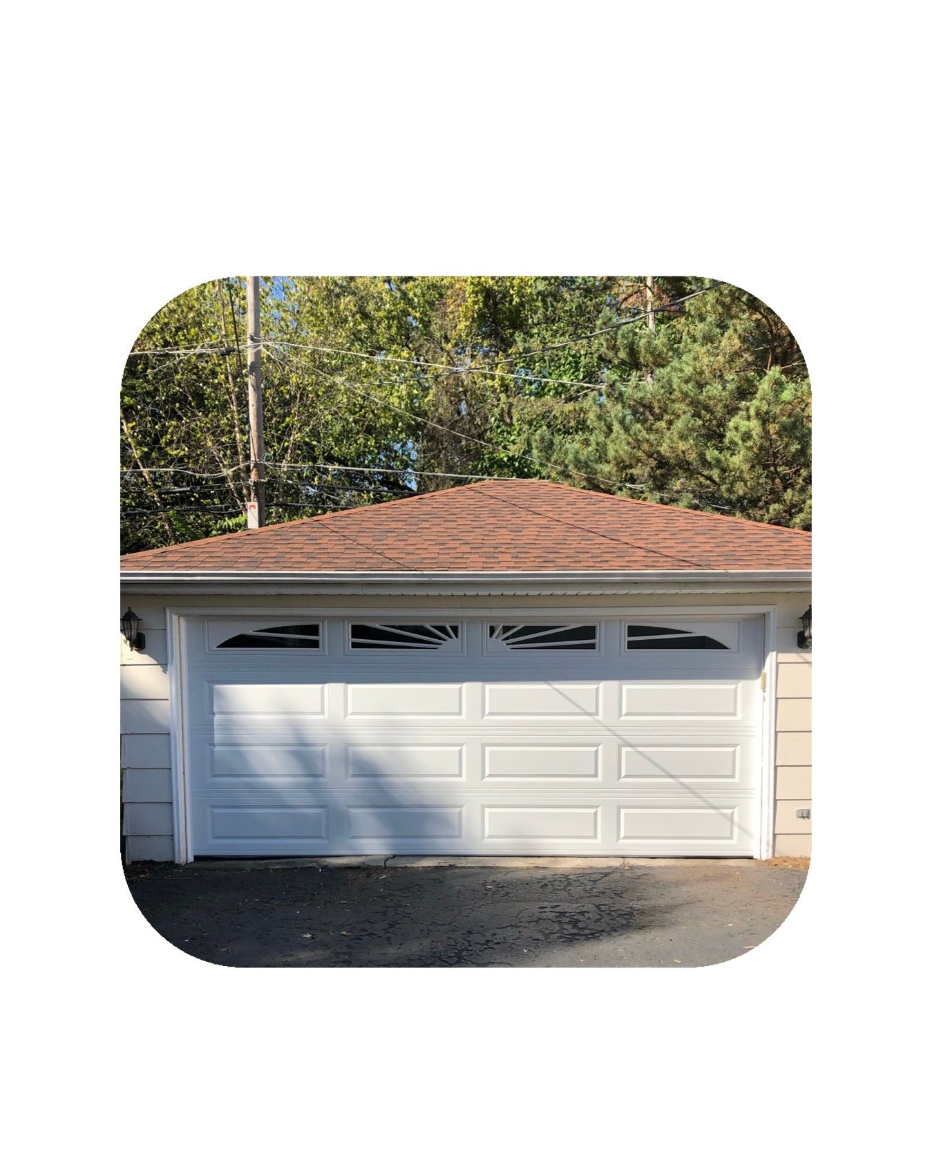 White garage door with brown roof, trees in the background.