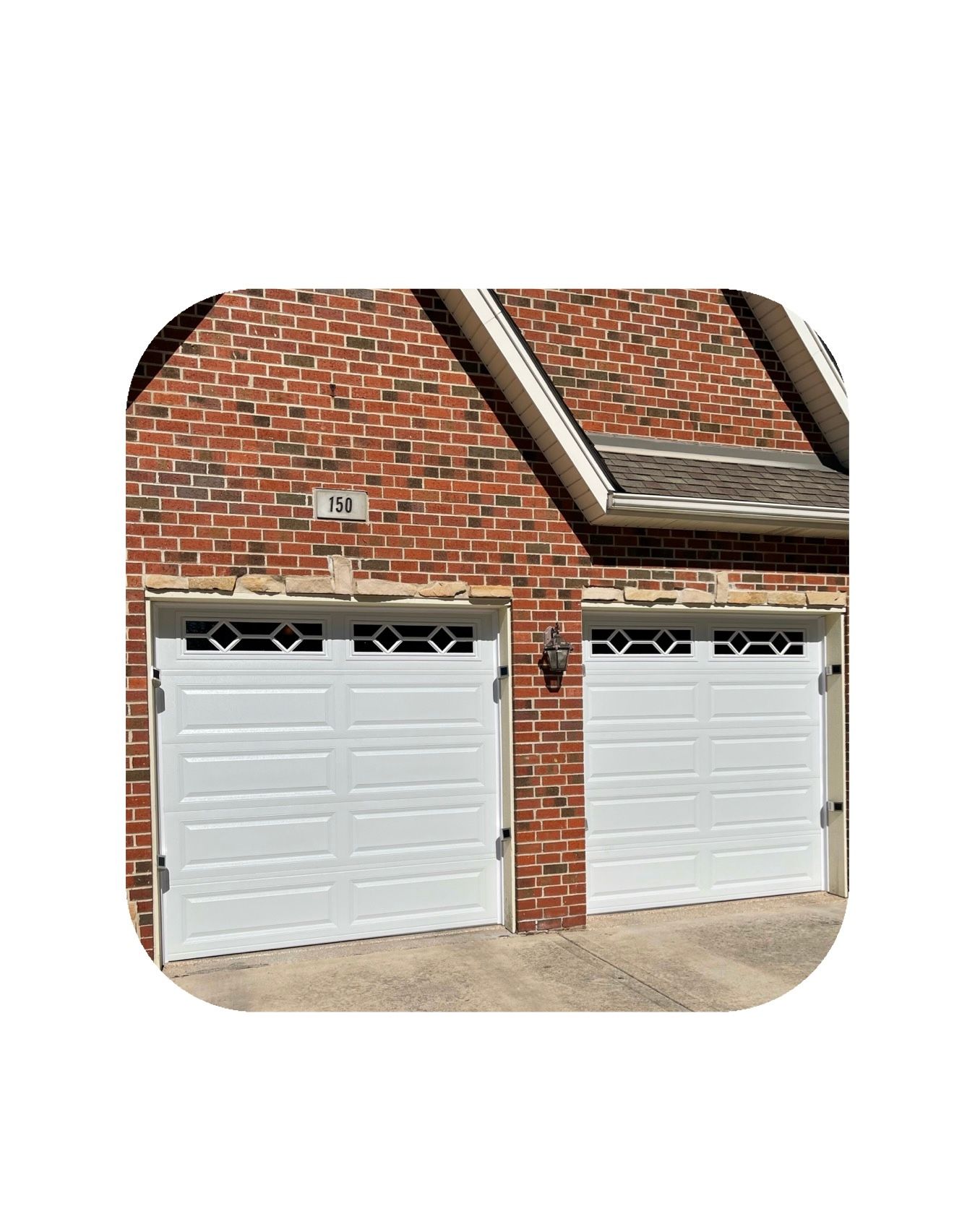 Two white garage doors on a brick house with decorative glass windows at the top.