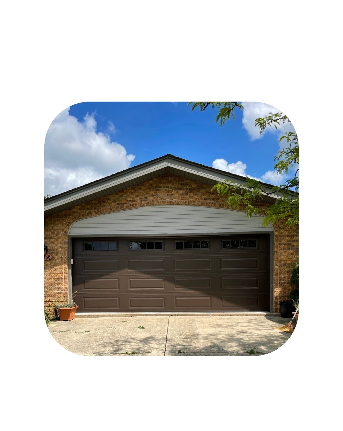 Brown garage door with windows under a brick facade, blue sky with clouds in background.