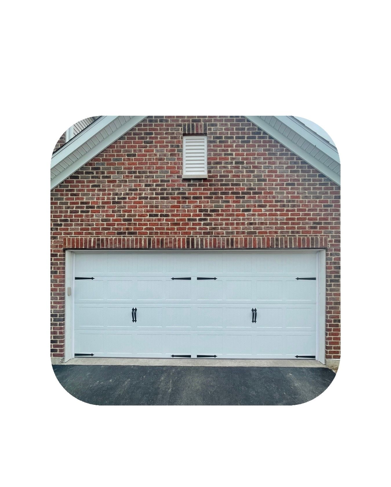 White garage door on brick building with black asphalt driveway.