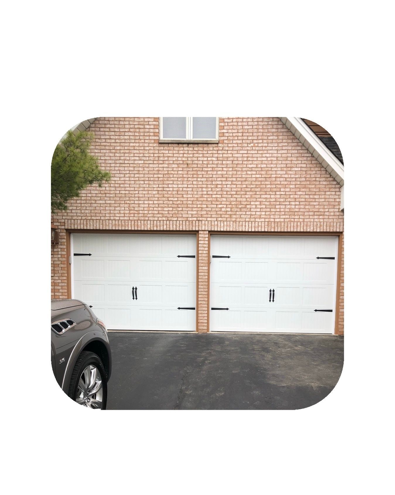 Two white garage doors on a brick house, car parked in front.