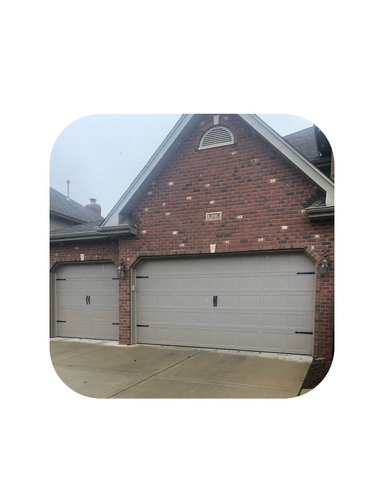 Garage with two doors, tan colored, brick exterior, gray sky.