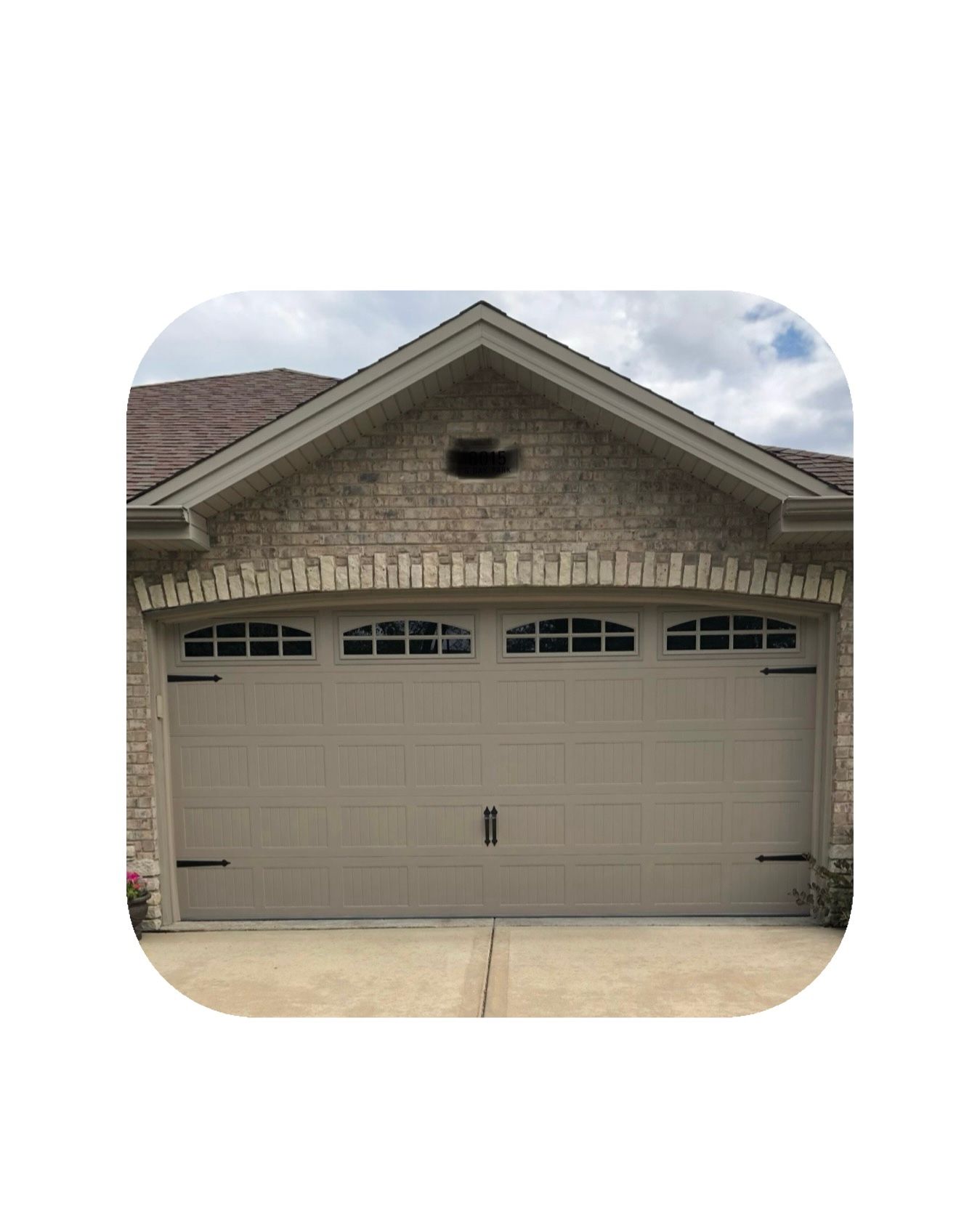 Tan garage door with windows, in front of a brick facade.