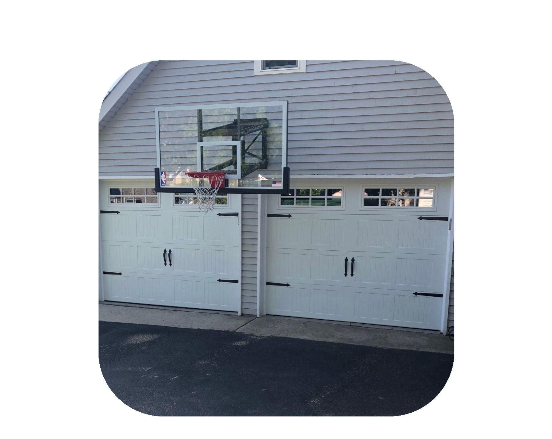 Basketball hoop mounted above a white garage door, asphalt driveway.