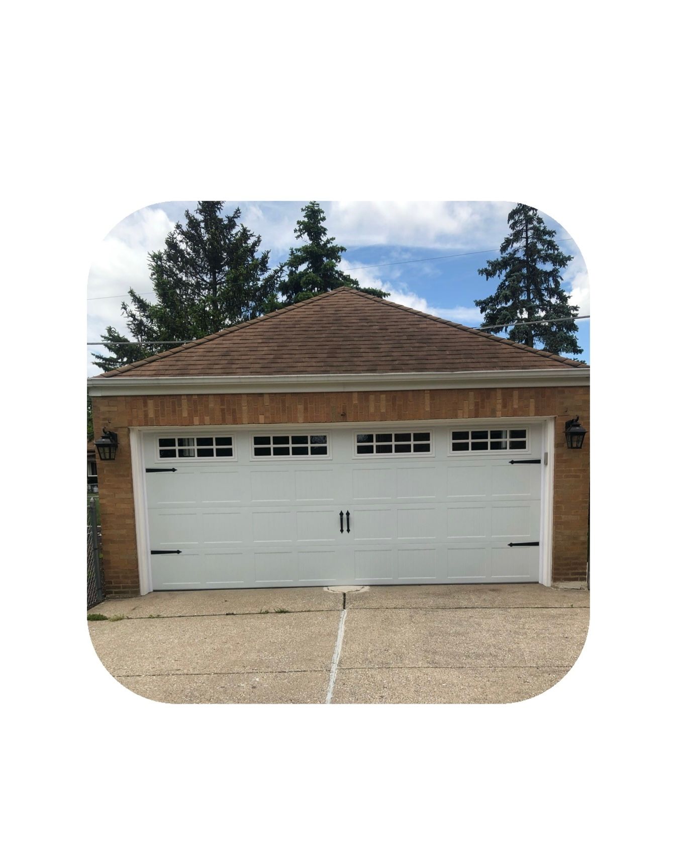White garage door with windows, brick building, brown roof, and trees.