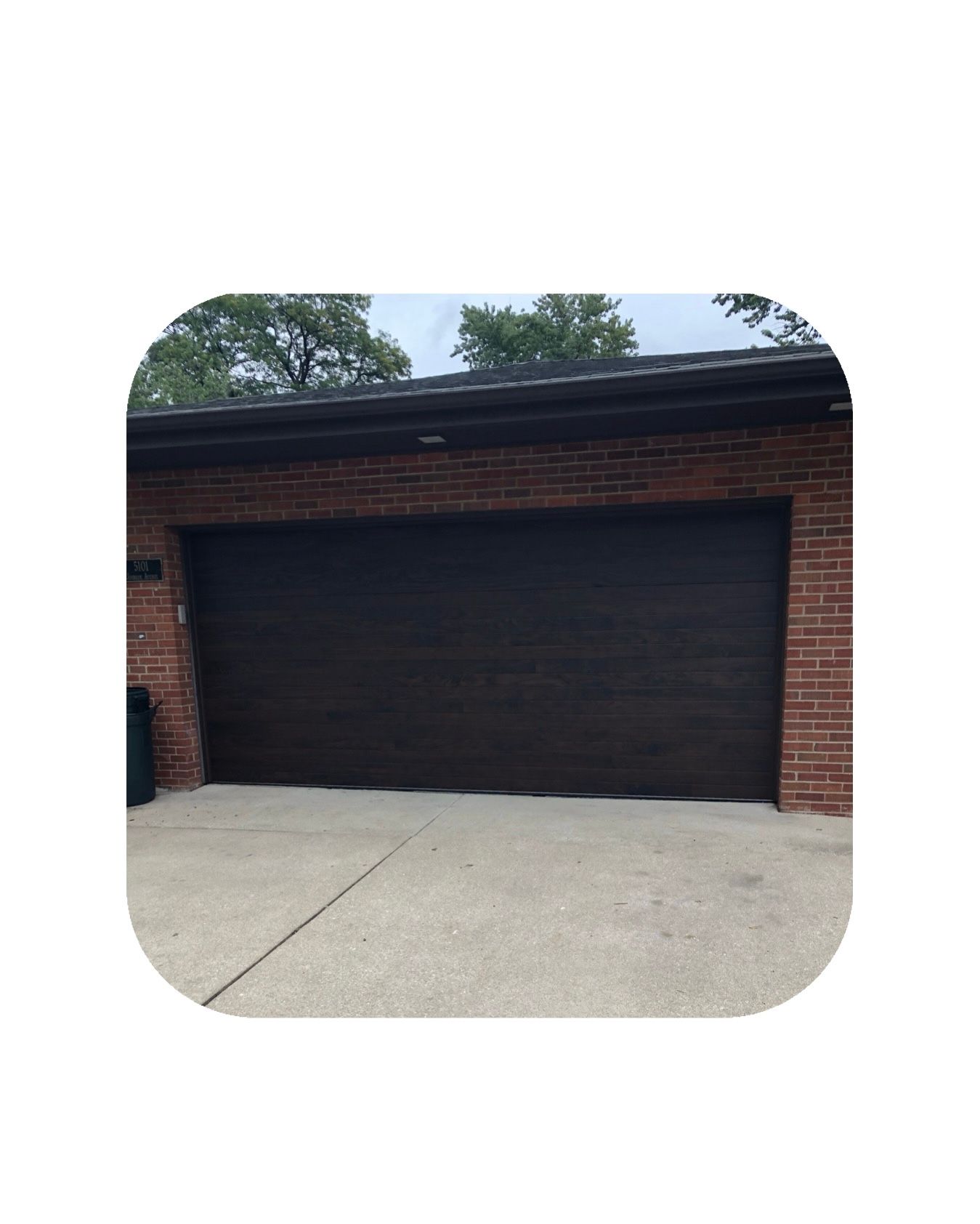 Brown garage door on a brick building with a concrete driveway.