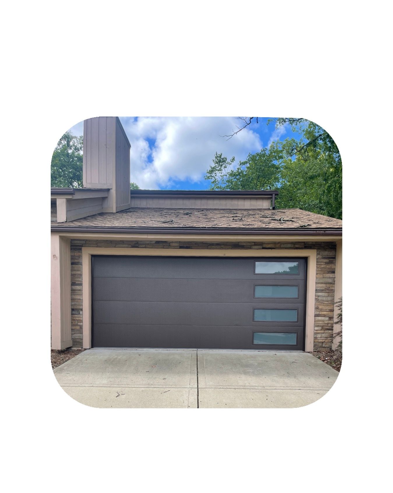 Brown garage door with frosted windows, set in a stone and tan building, cloudy sky background.