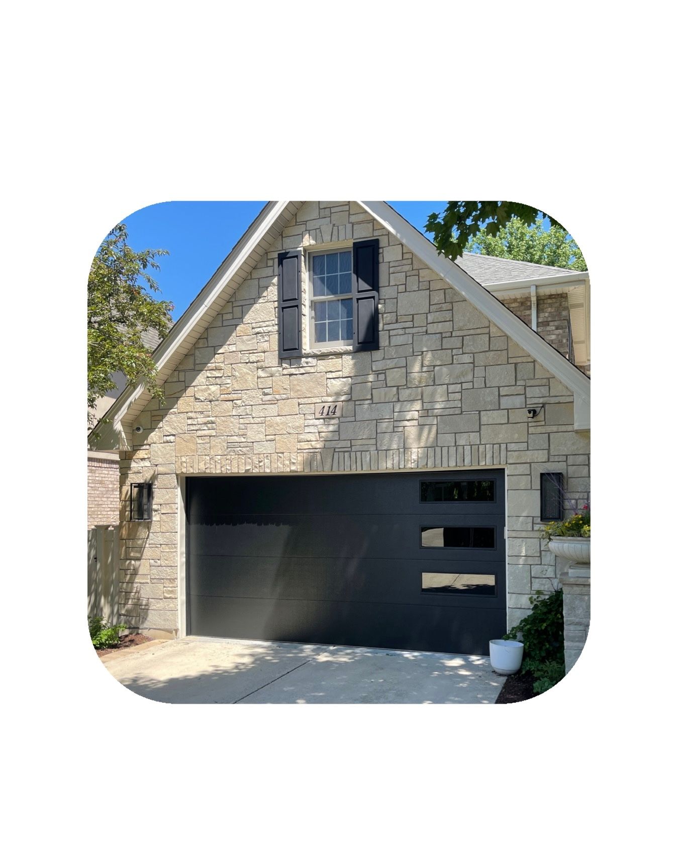 Garage with black door, stone facade, small window with black shutters.