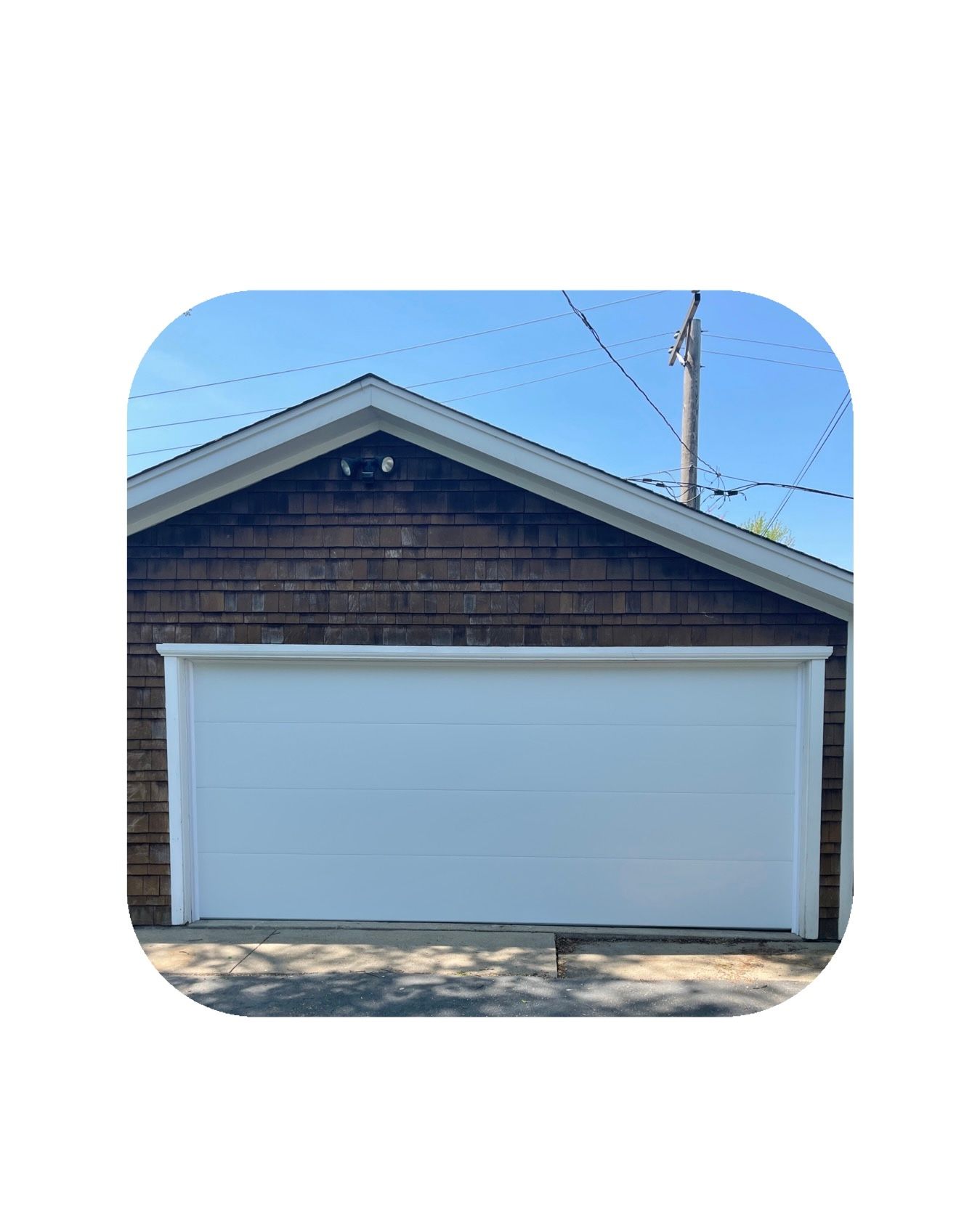 White garage door on brown shingled building with blue sky background.