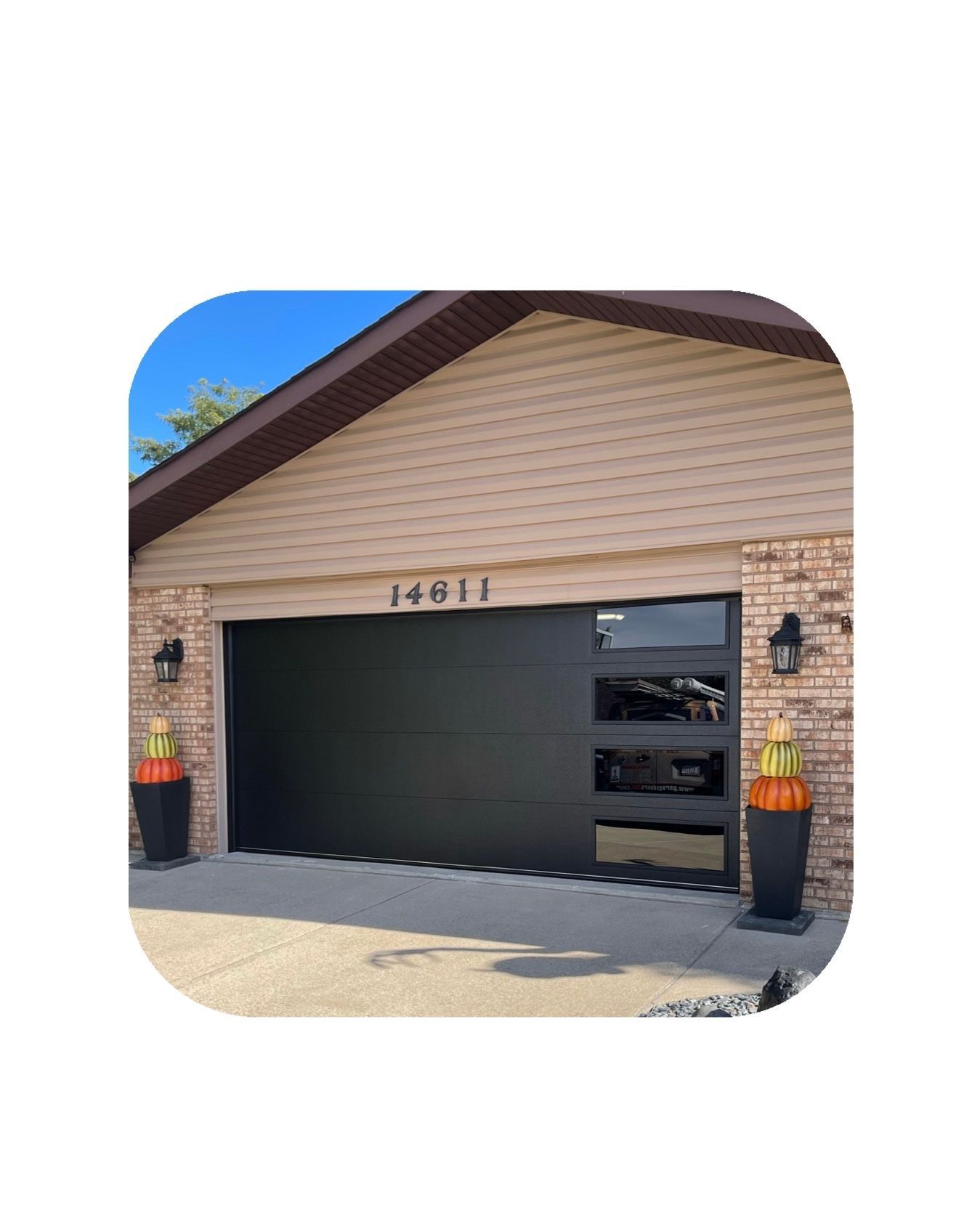Black modern garage door with glass panel, brick and tan siding, address 