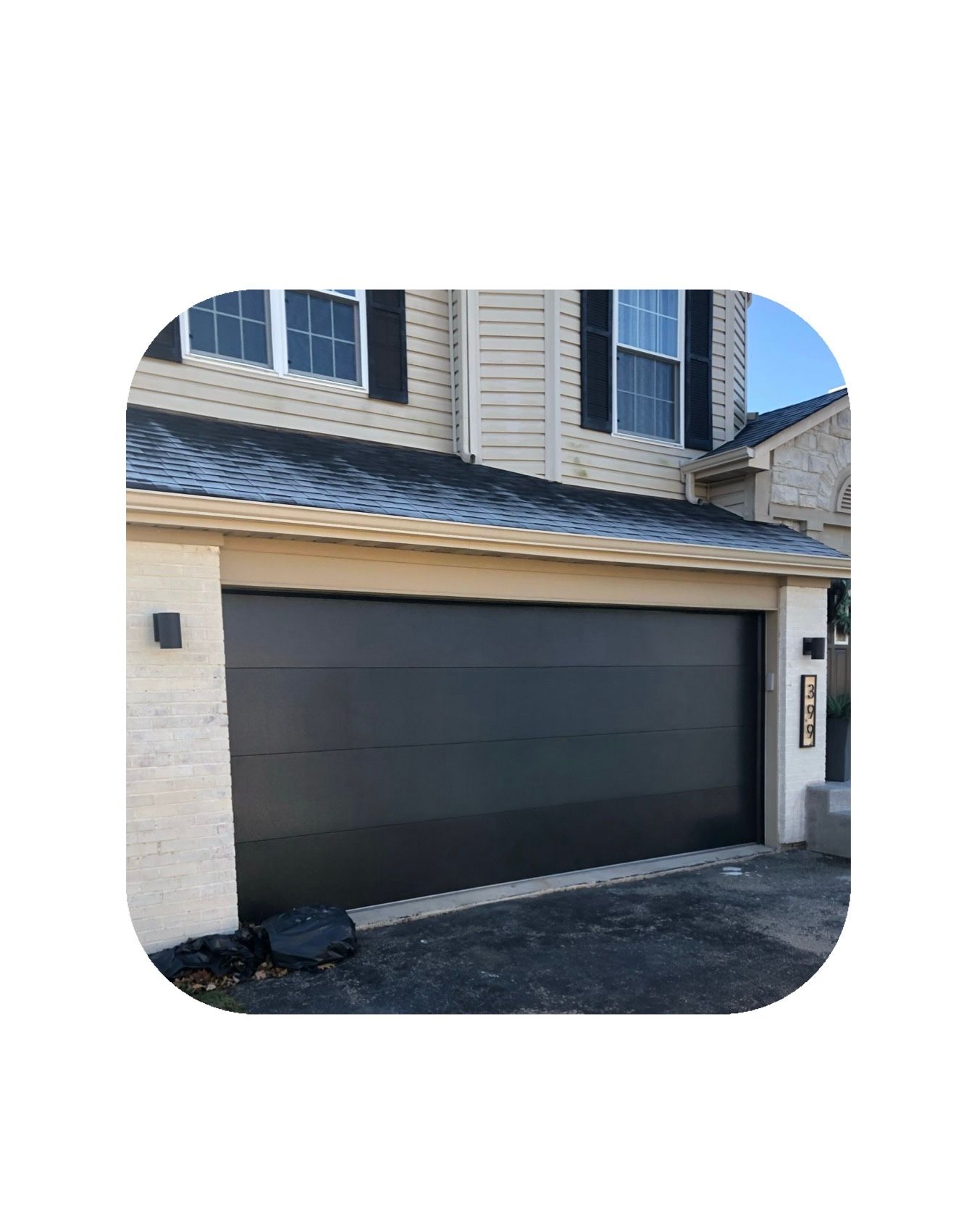 Black garage door on a tan house with a dark roof and black shutters.