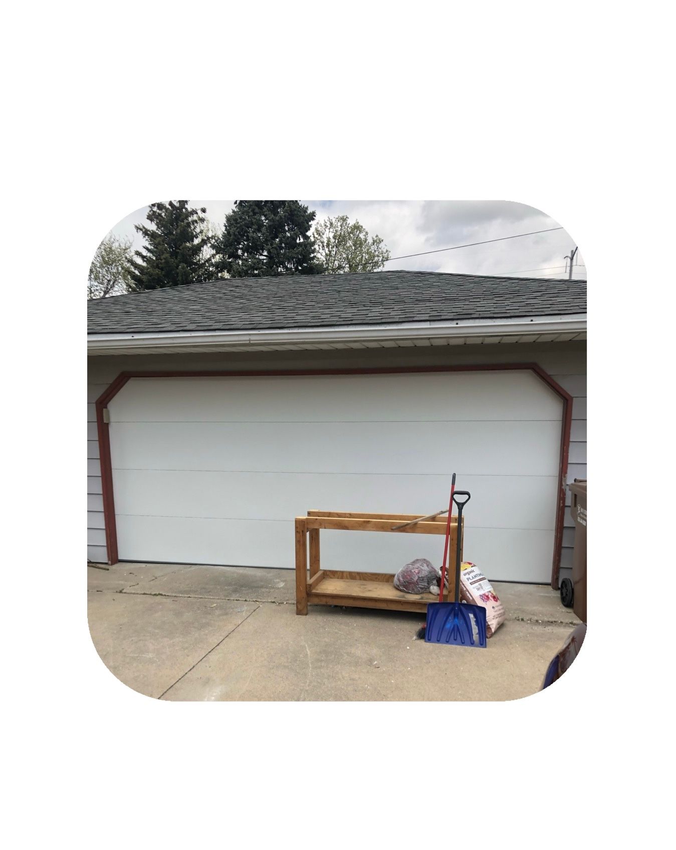 Garage with wooden workbench, bags, and hand truck on driveway.