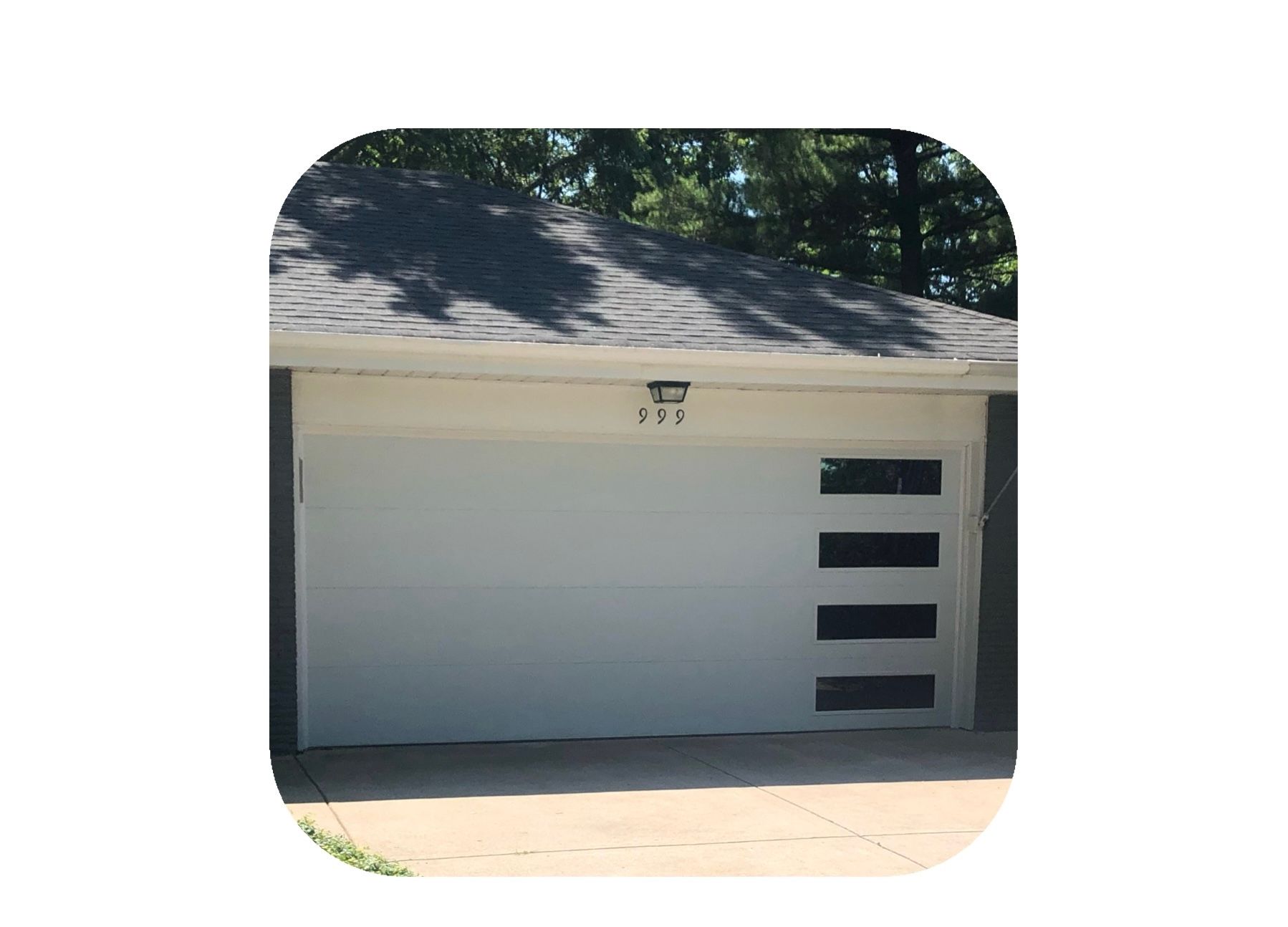 White garage door with four horizontal black windows. The roof and trees are visible in the background.