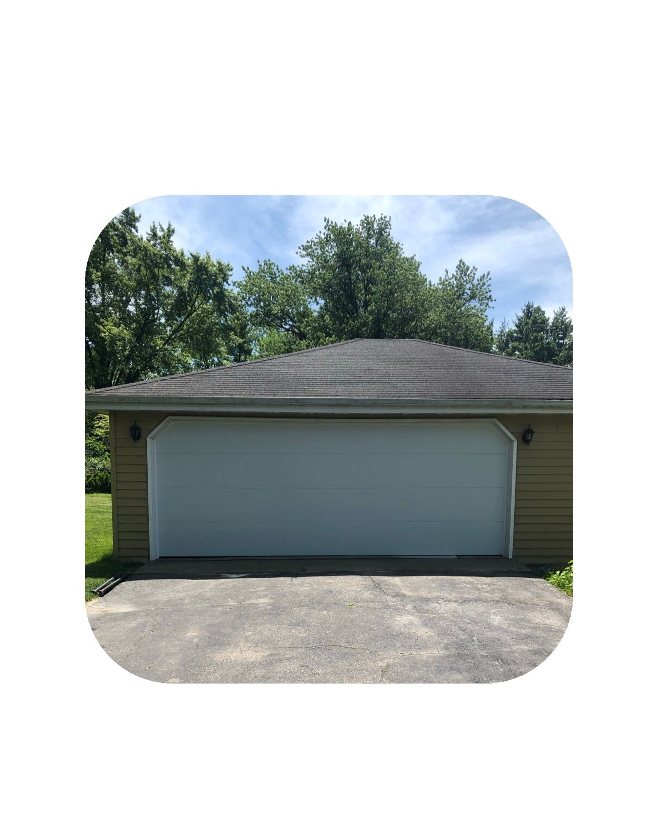 White garage door on a light green building with asphalt driveway and trees against a blue sky.
