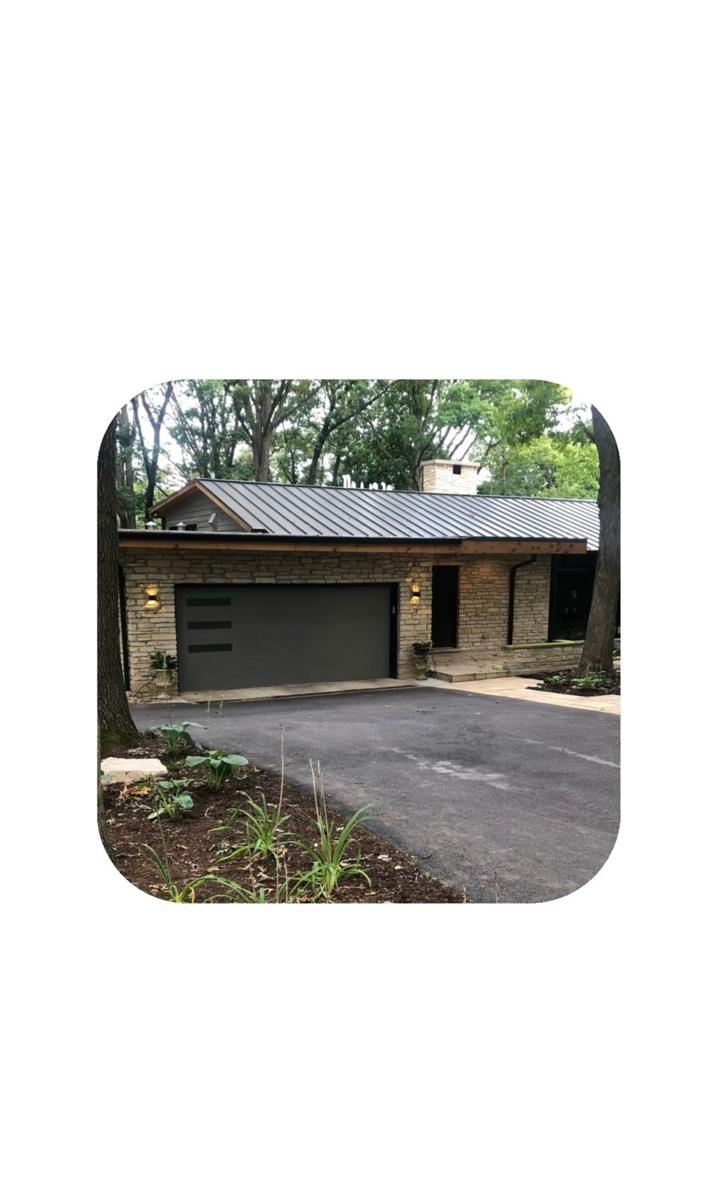 Stone house with gray garage door, black asphalt driveway, and metal roof.