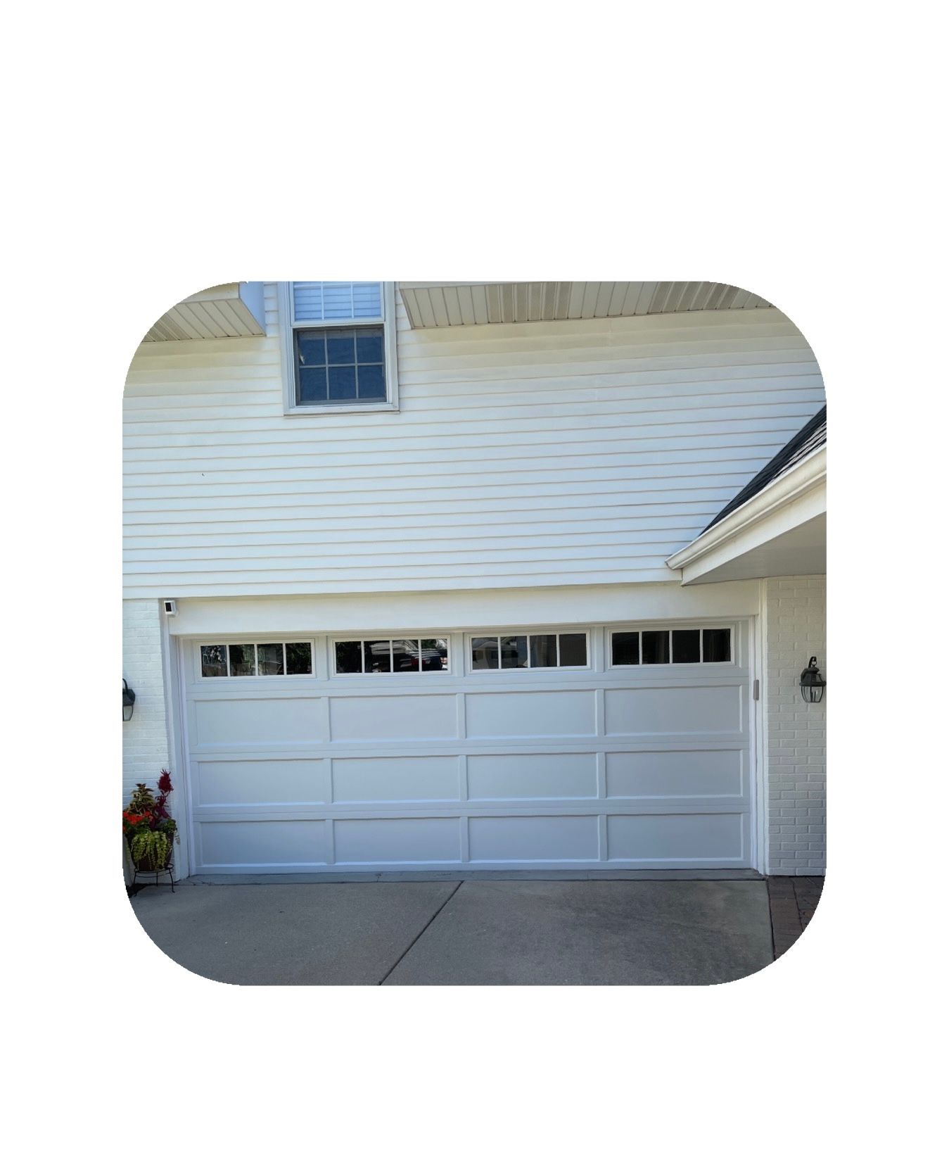 White garage door with rectangular windows, beneath white siding and a small window.