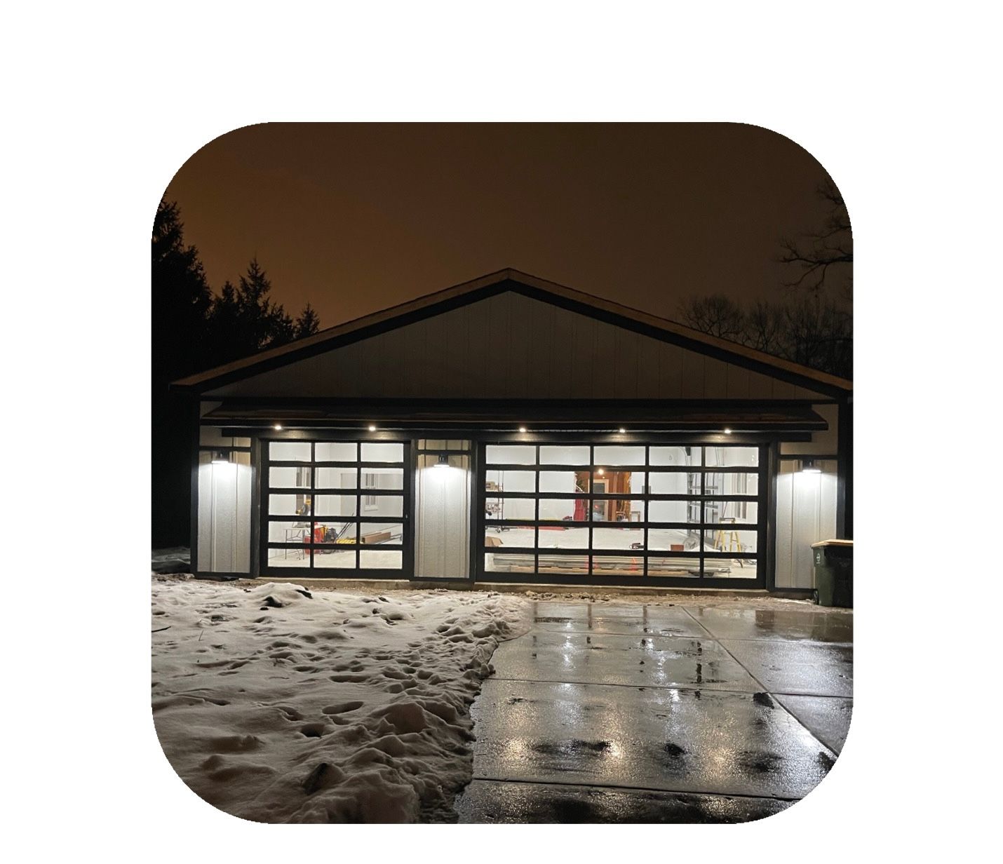 Garage with glass doors, illuminated at night with snow on the ground.