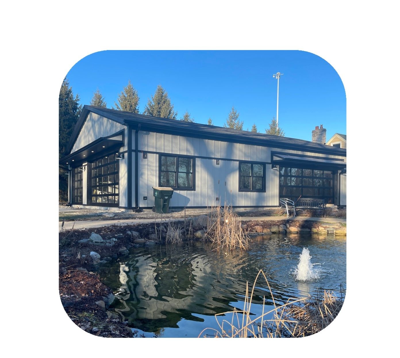 Building with glass garage doors by a pond with fountain.