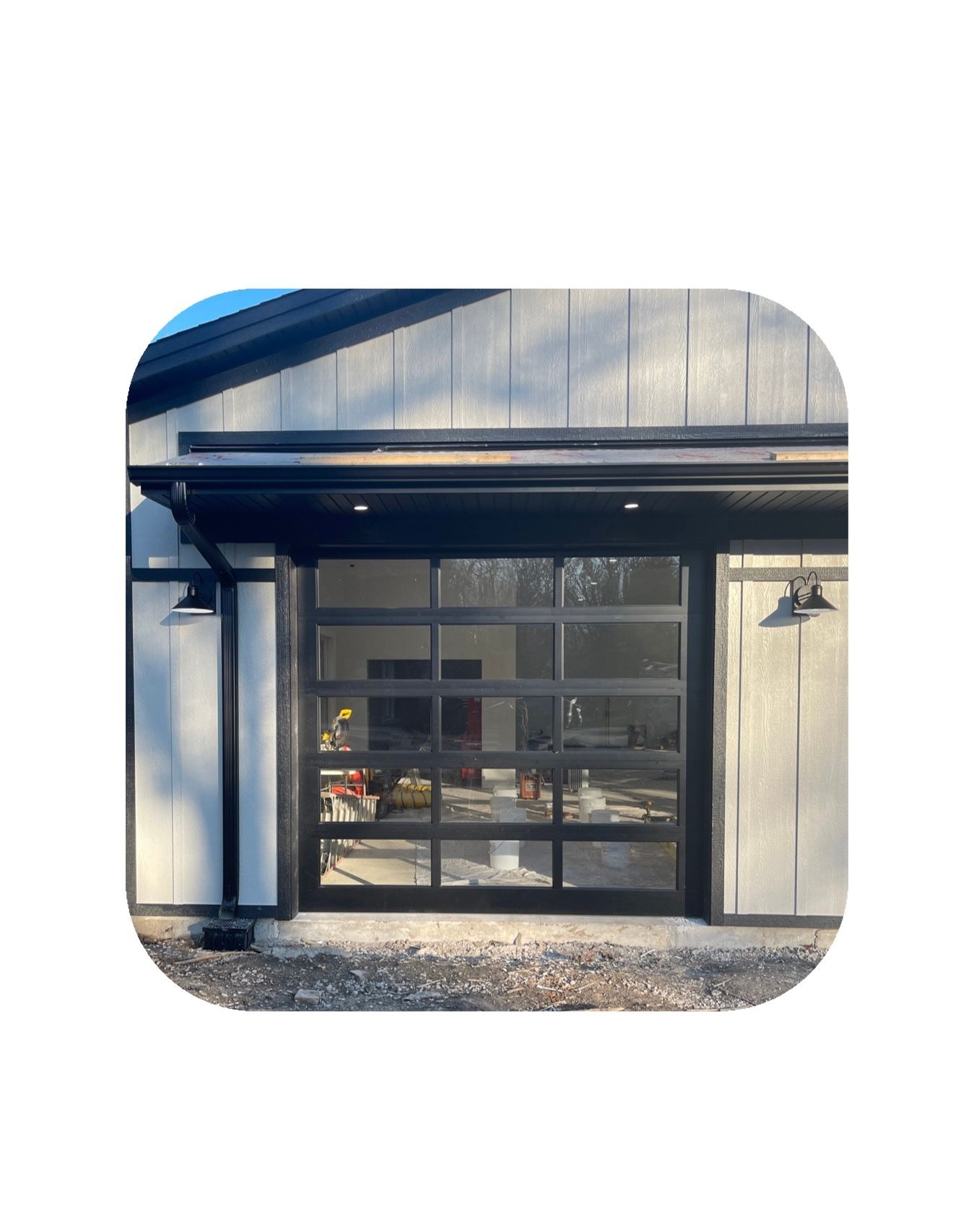 Black-framed glass garage door on a white building, with black trim and two outdoor lights.