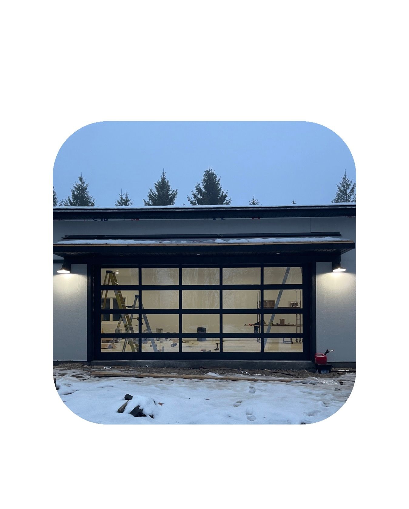 Glass garage door, black frame, snowy ground, trees in the background, overcast sky.