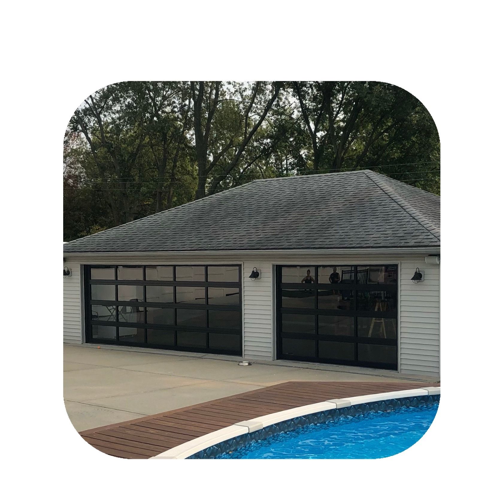 Garage with two glass doors, next to a pool. Black frames, light siding, and gray roof.