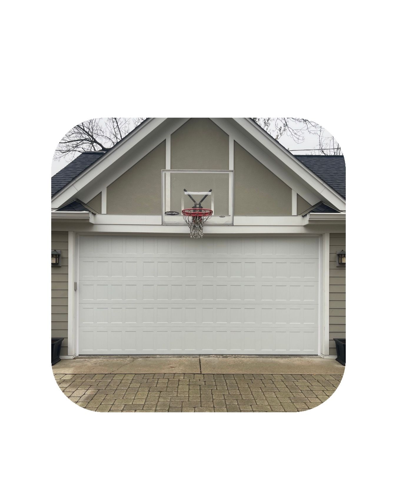 White garage door with basketball hoop, house exterior with brick paving.