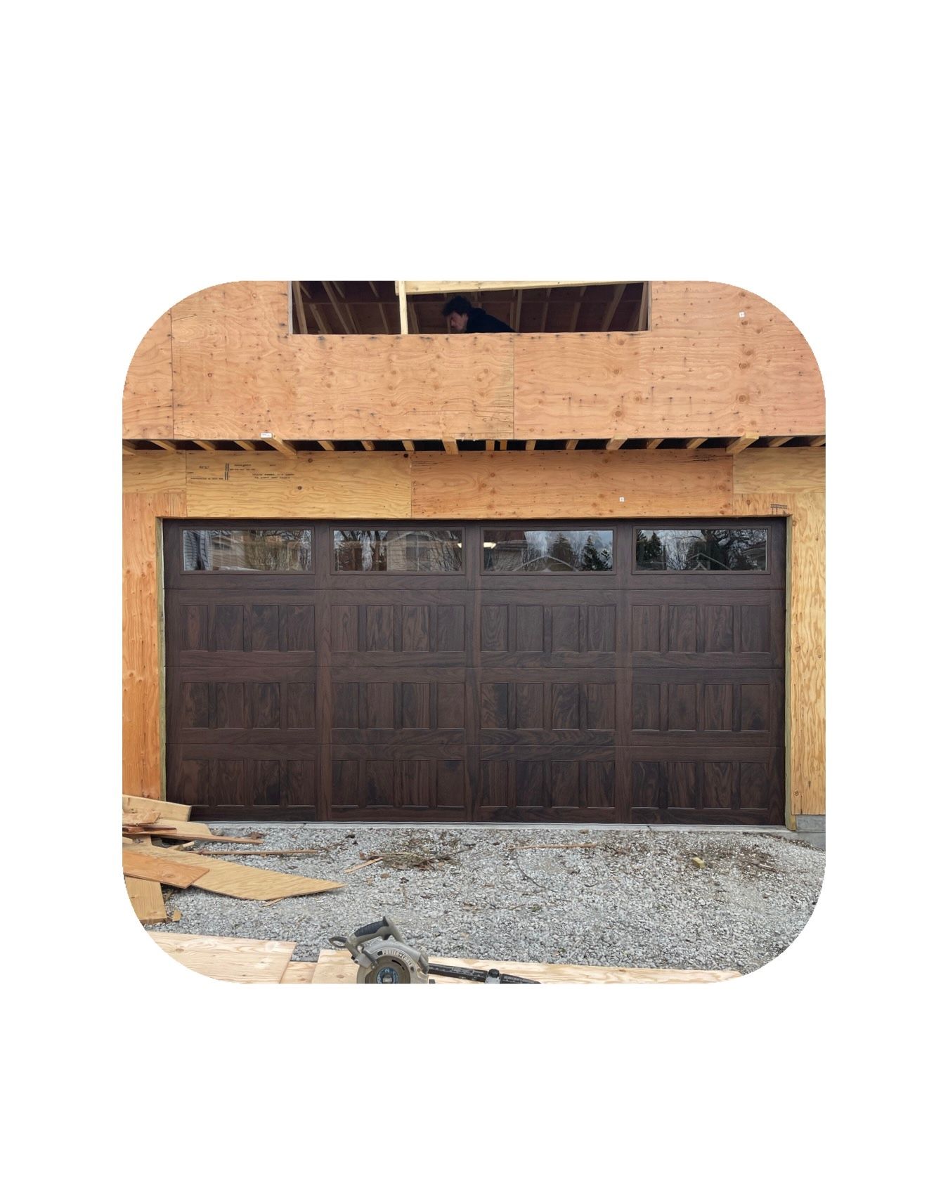 Brown garage door with windows, under construction, set in a wooden frame with gravel ground.