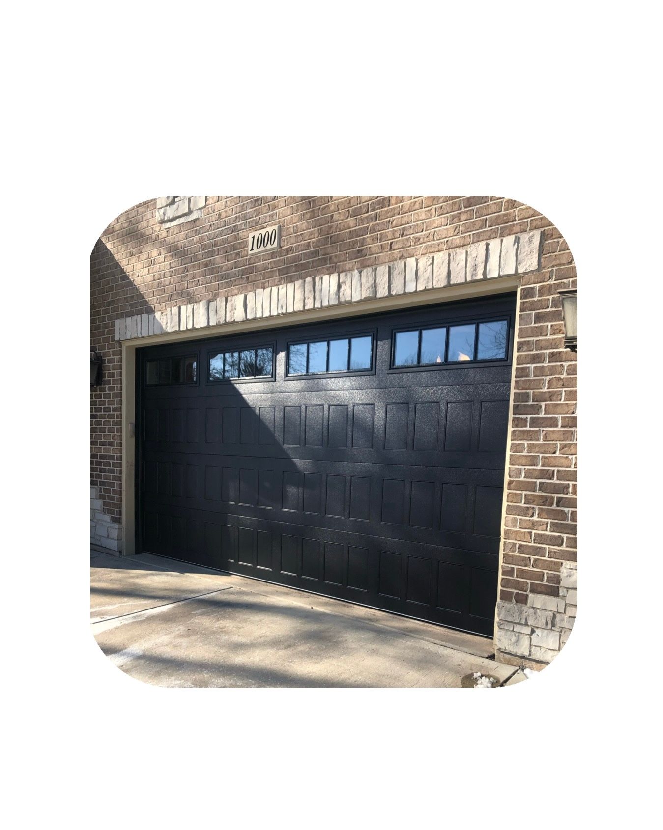 Black garage door with windows, set in a brick and stone facade.