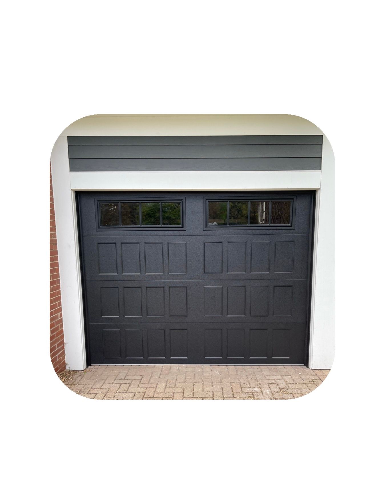 Black garage door with glass windows, gray trim, and brick driveway.