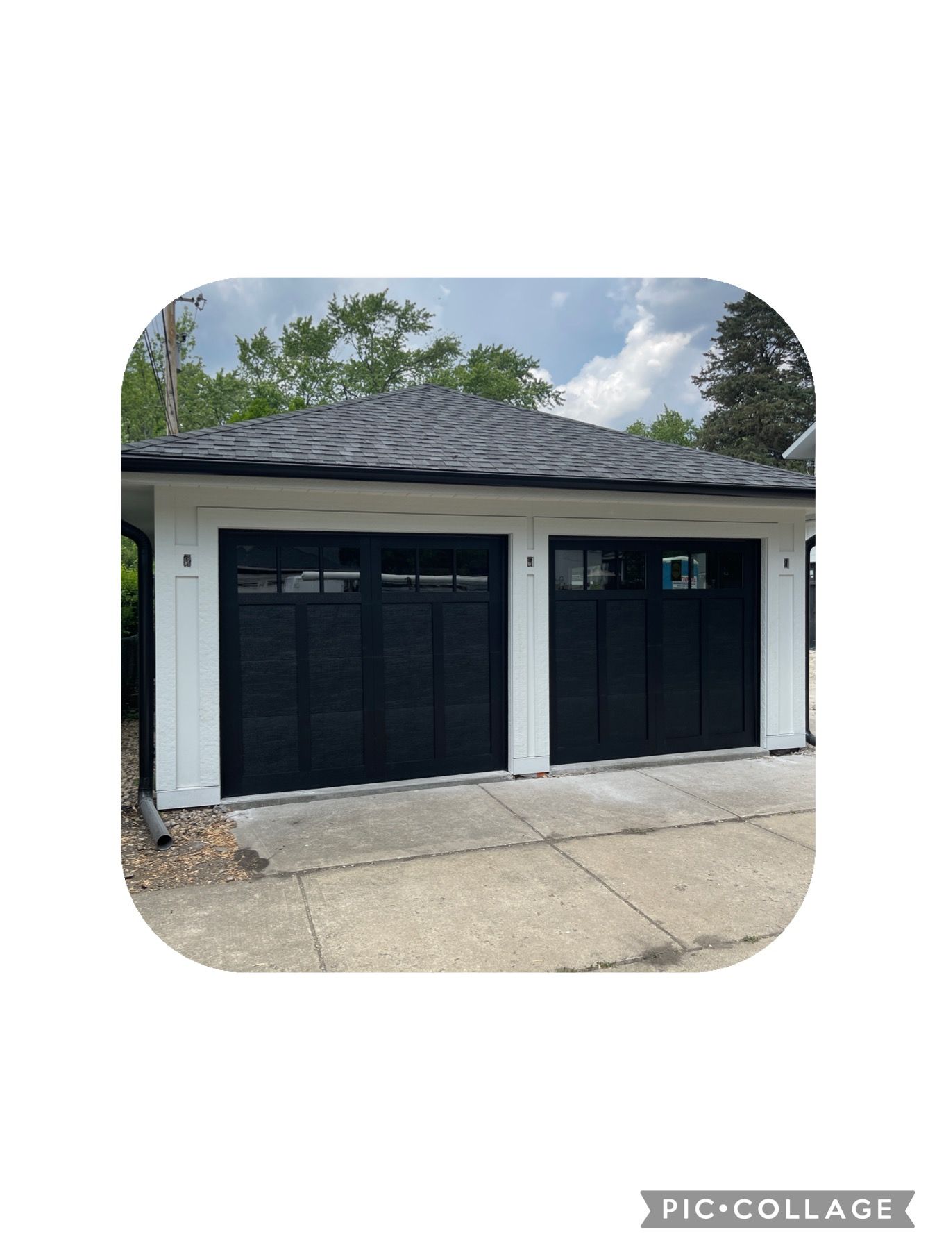 Two-car garage with black doors and white trim. Gray roof, concrete driveway, and a cloudy sky.