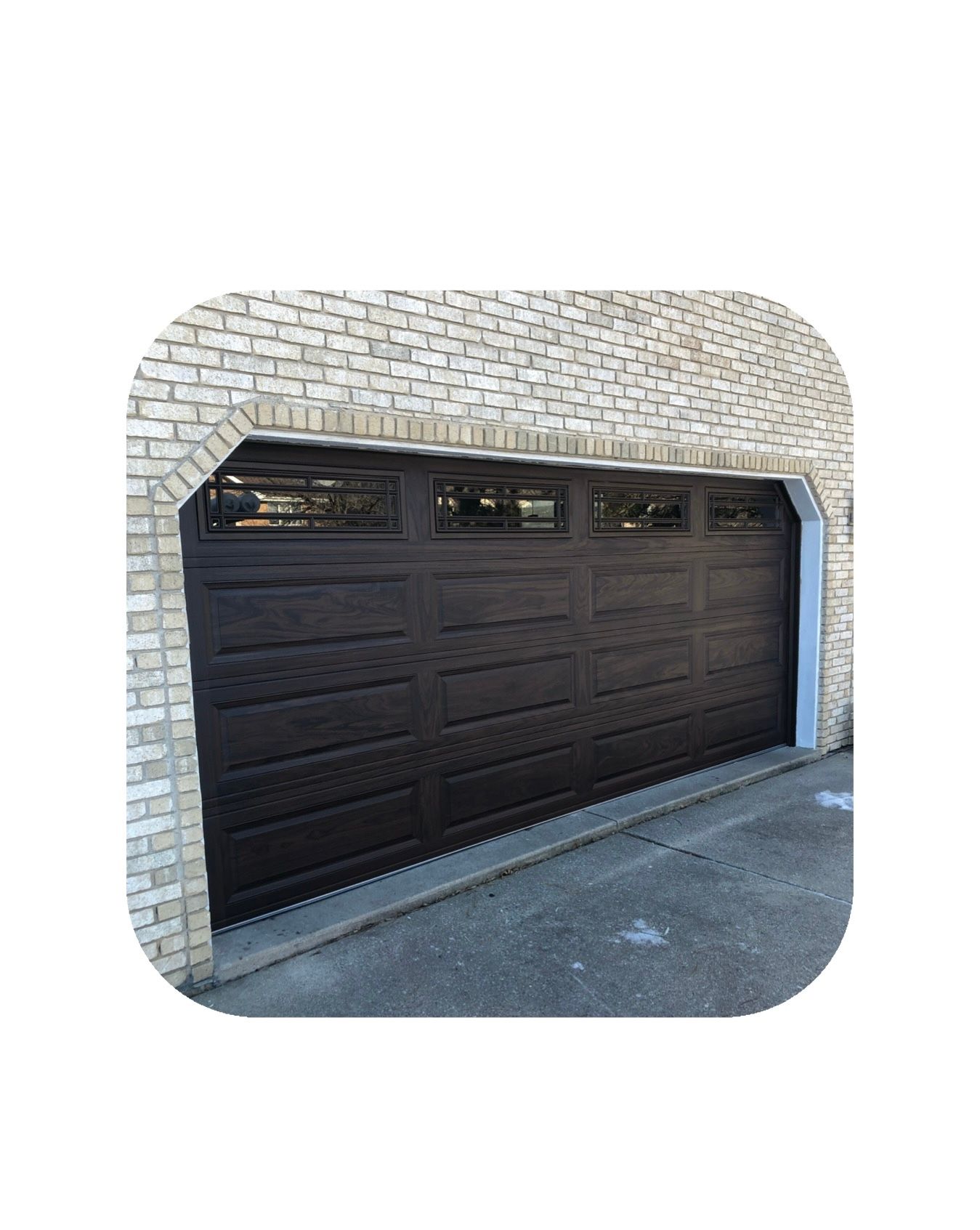 Dark brown garage door with small glass panels, set in brick archway.