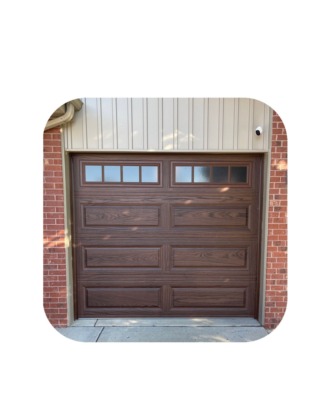Brown wooden garage door with windows, flanked by brick, under beige siding.