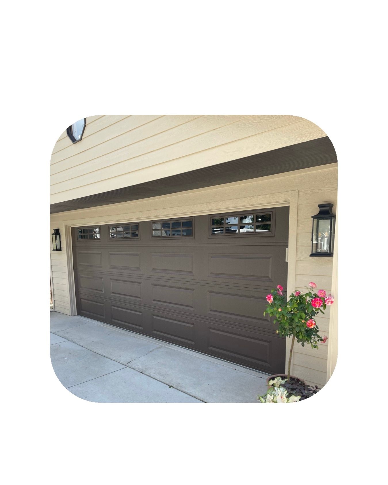 Brown garage door with windows, on a beige house, with potted flowers on the side.