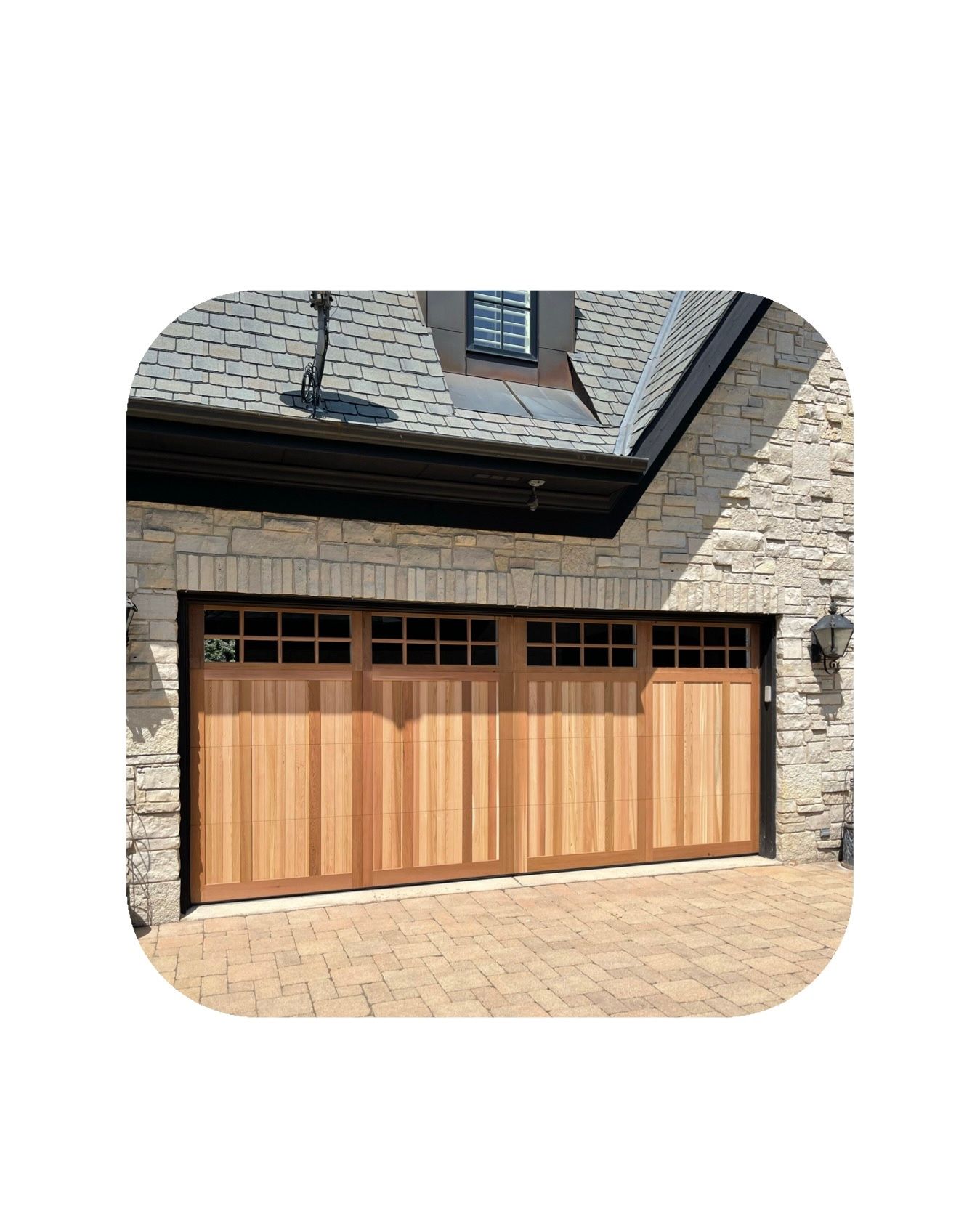 Wooden garage door with window panels, brick exterior, and stone walkway.