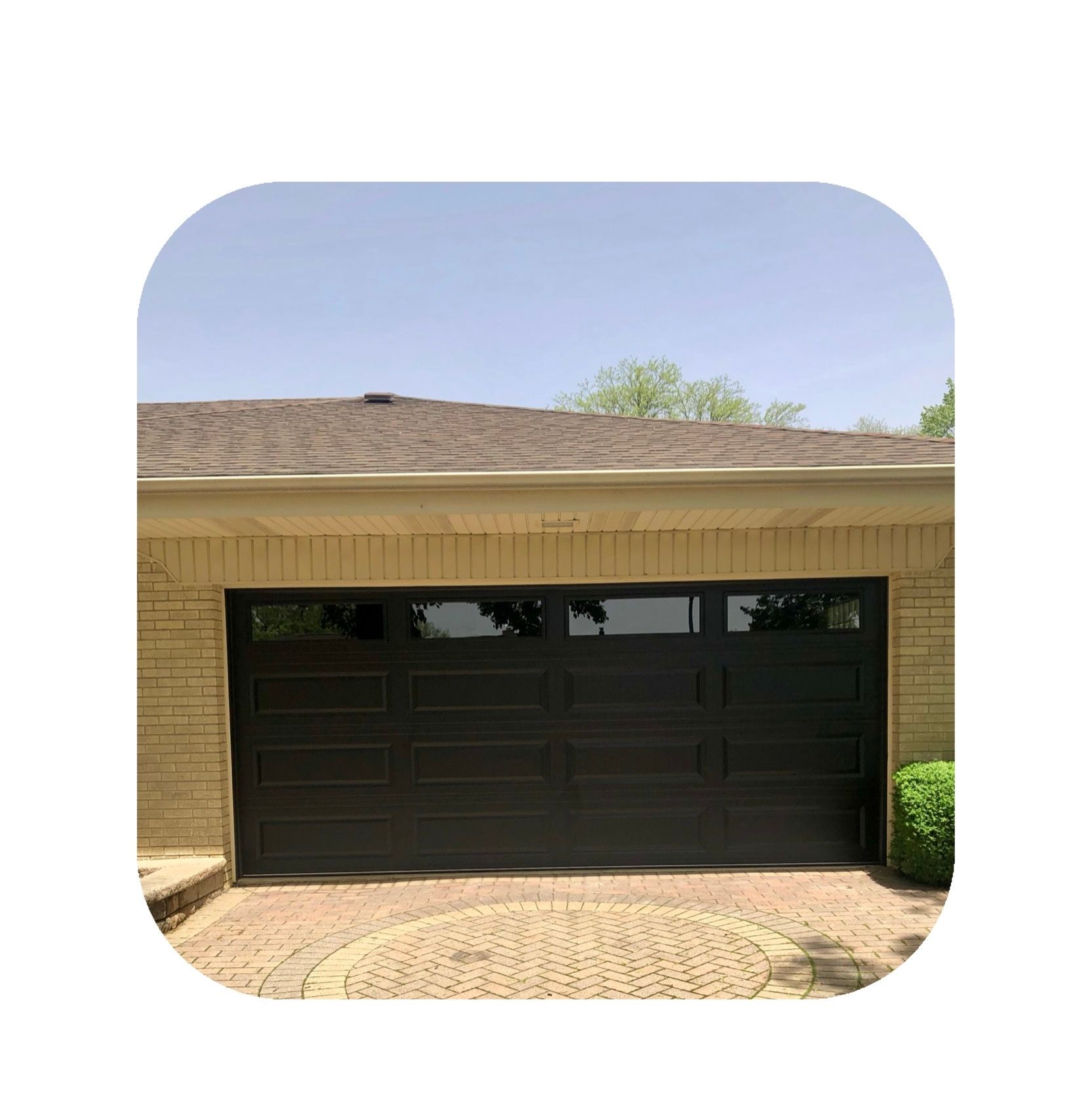 Black garage door with frosted windows, beige brick building, and brick driveway.