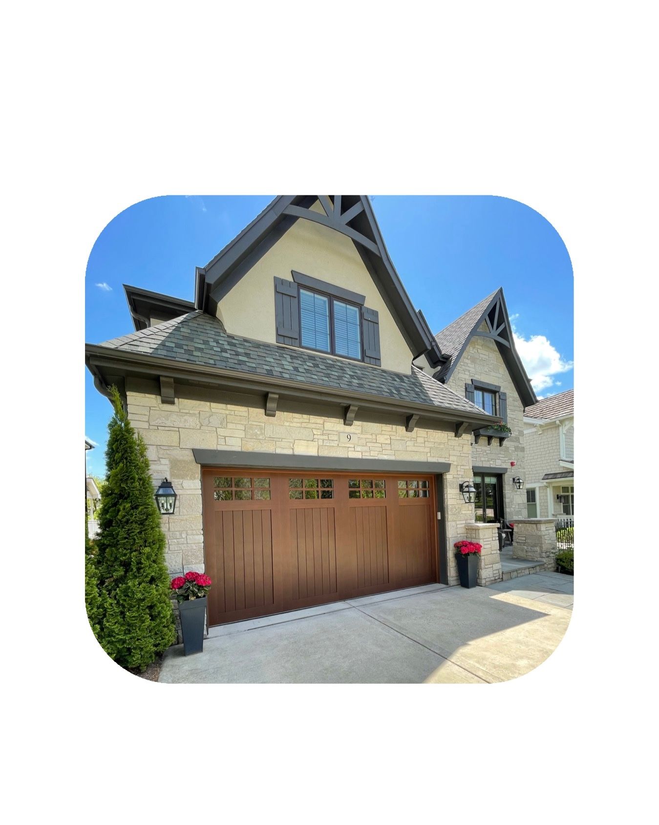 Tan brick home with a wooden garage door, windows, and decorative stone accents. Blue sky.