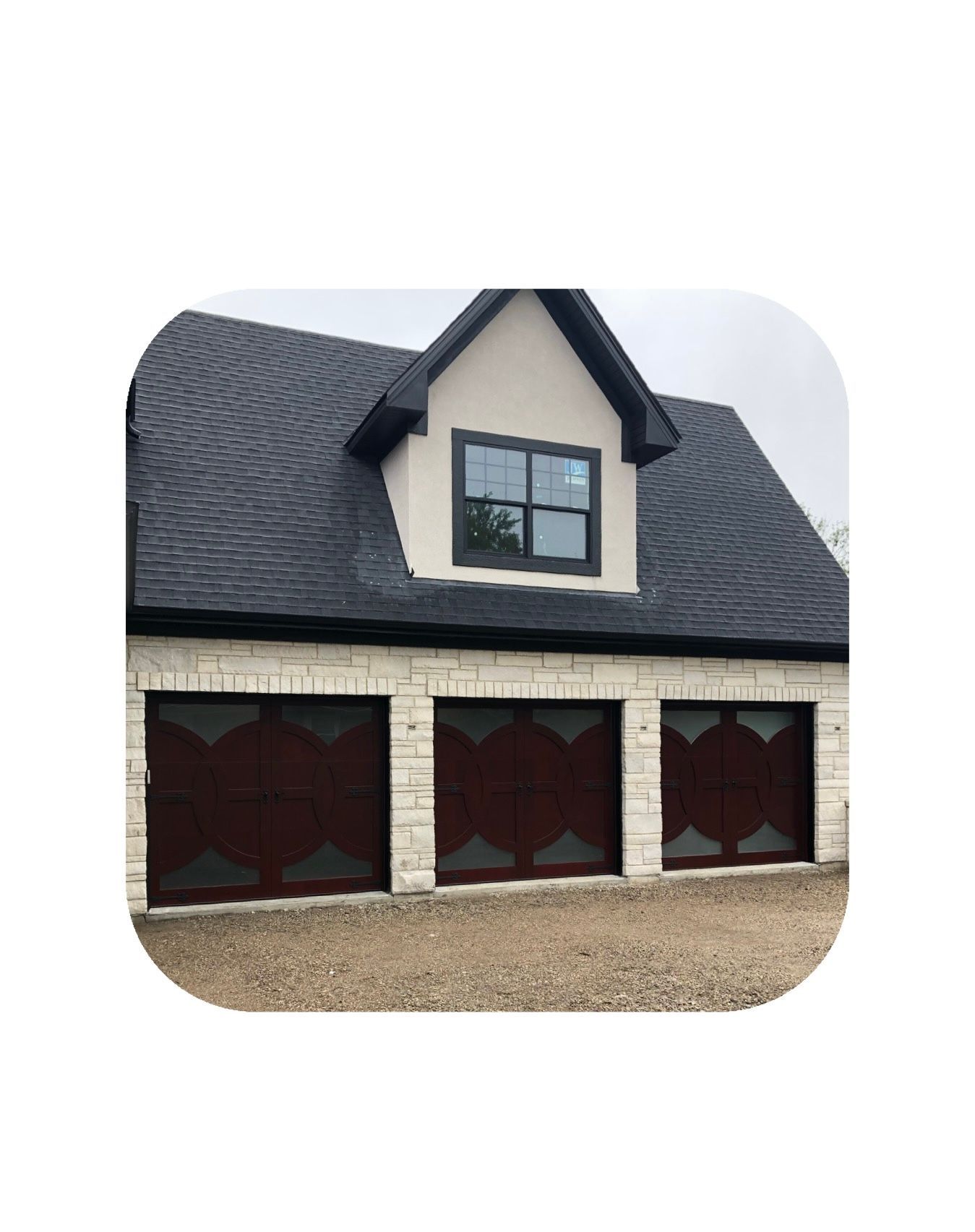 Three-bay garage with dark brown doors and white stone exterior; black roof with small windowed dormer.
