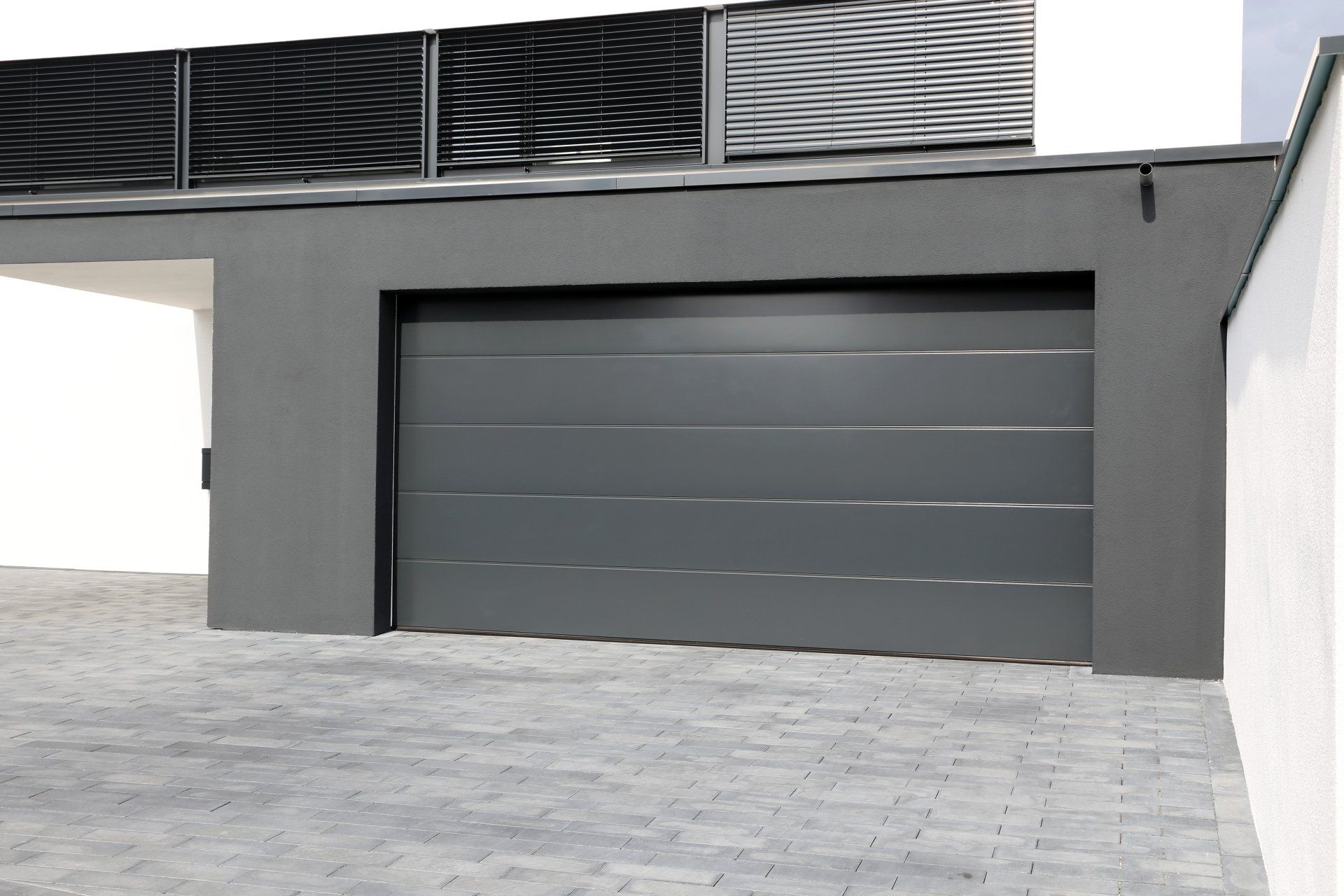Gray garage door on a modern gray building with a paved driveway.