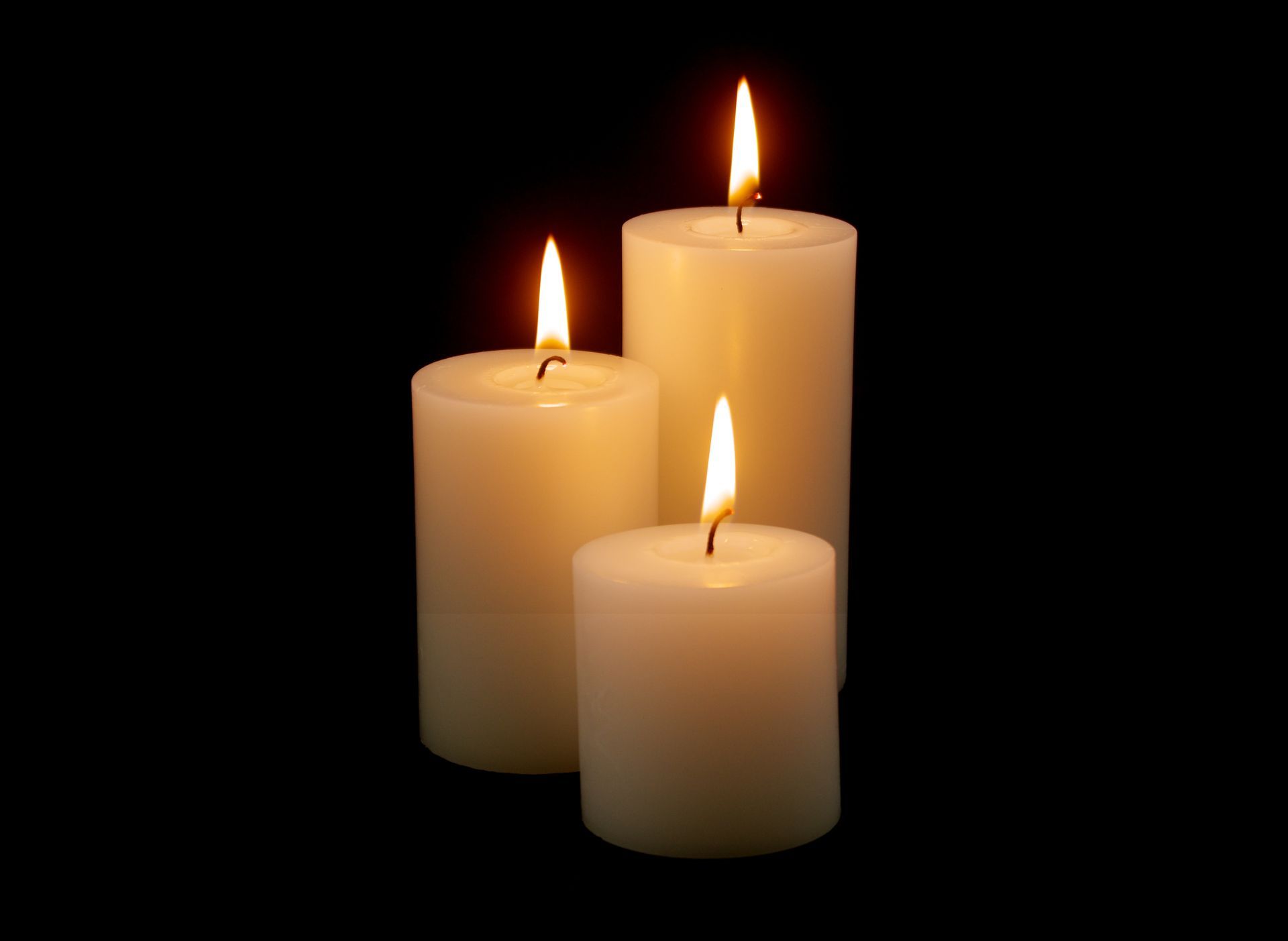 Three white pillar candles of varying heights glow against a solid black background.