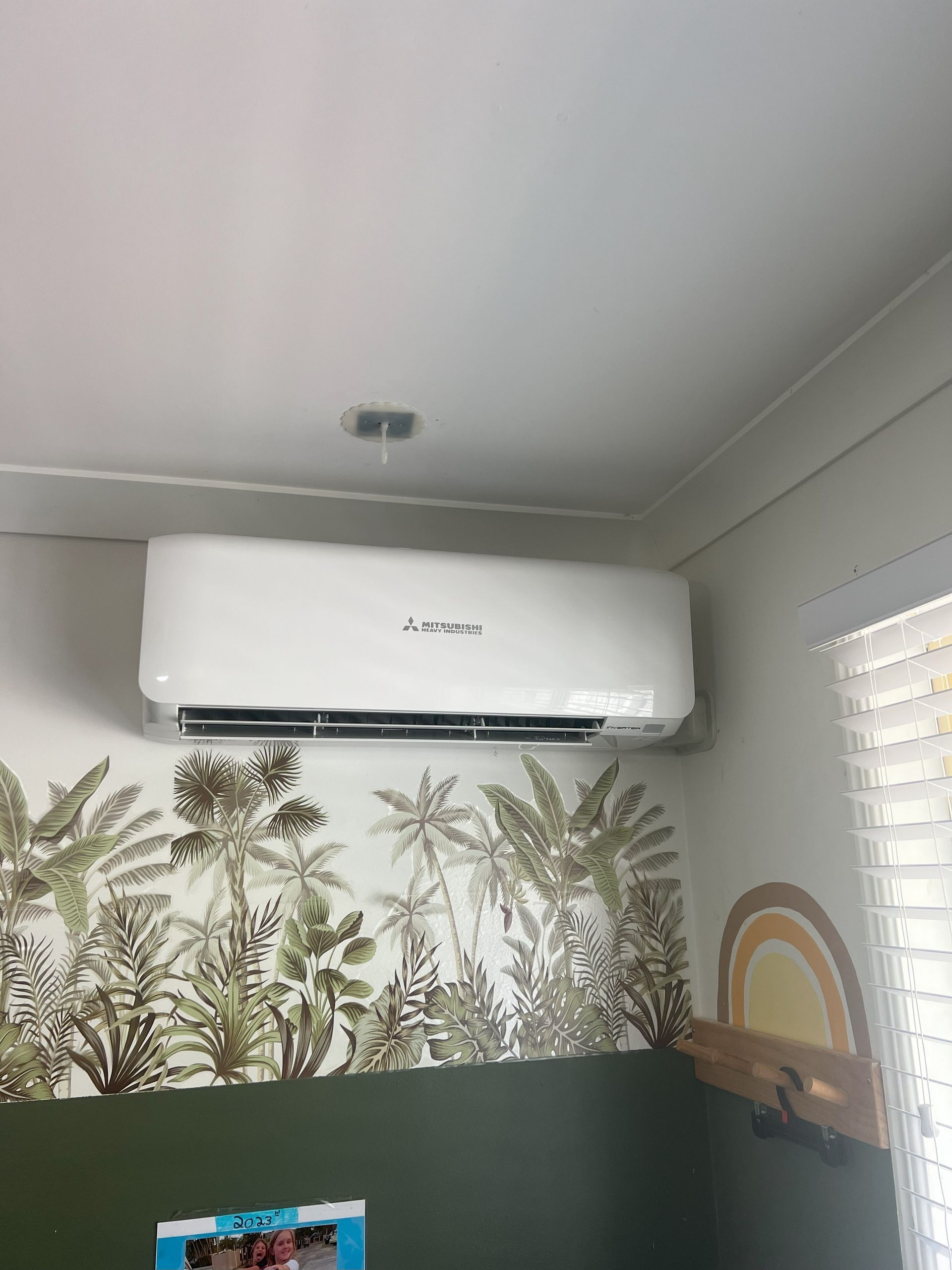 White Air Conditioner Unit Mounted on a Wall Above a Tropical Mural — NDR Trade Solutions in Robina, QLD