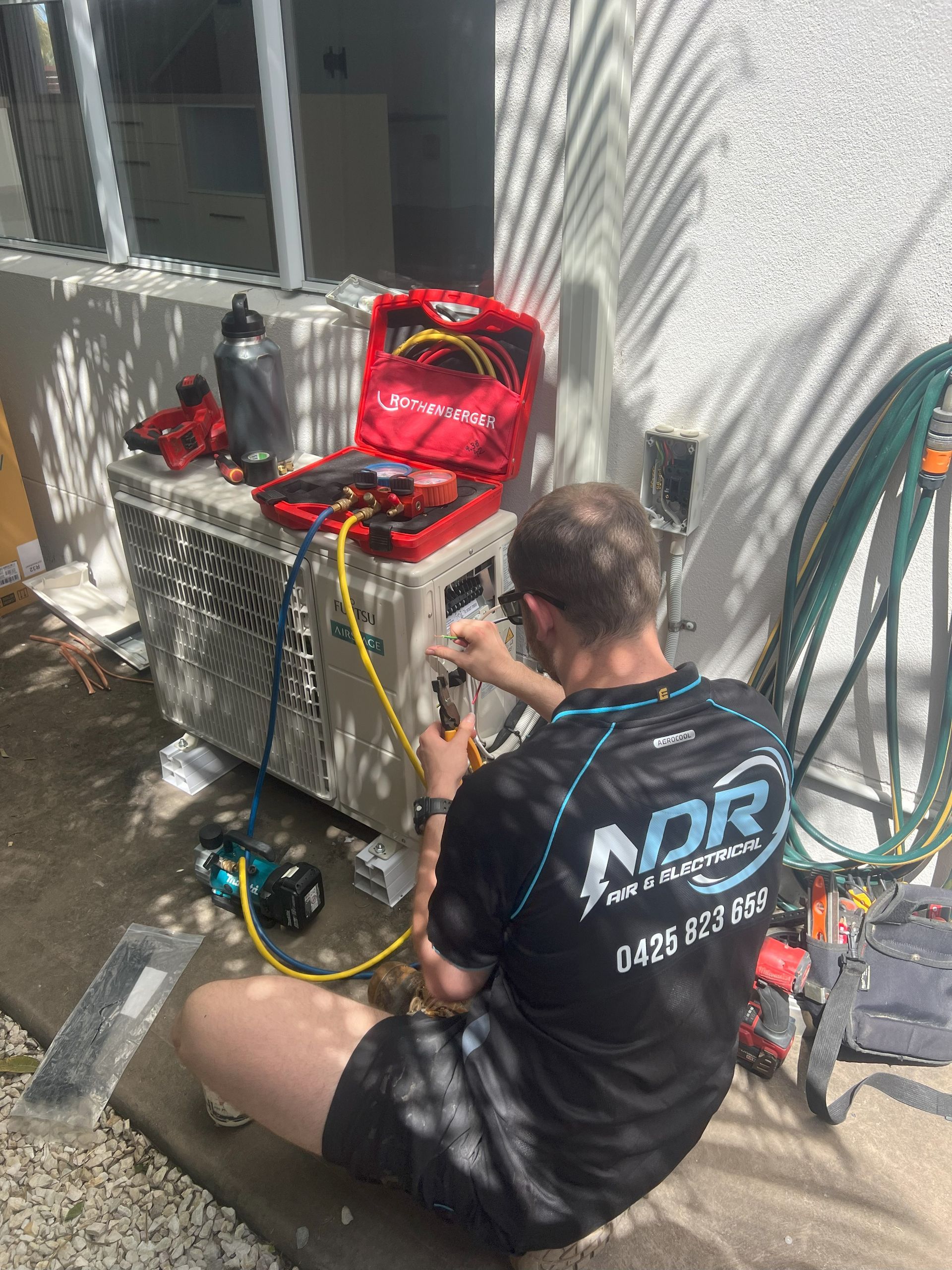 A Person Servicing an Ac Unit Outdoors, Using Tools — NDR Trade Solutions in Robina, QLD